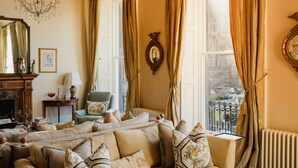 Ein gemütliches Wohnzimmer mit einem beigefarbenen Sofa, einem Kamin, einer Chandelüster und Blick auf einen Balkon.