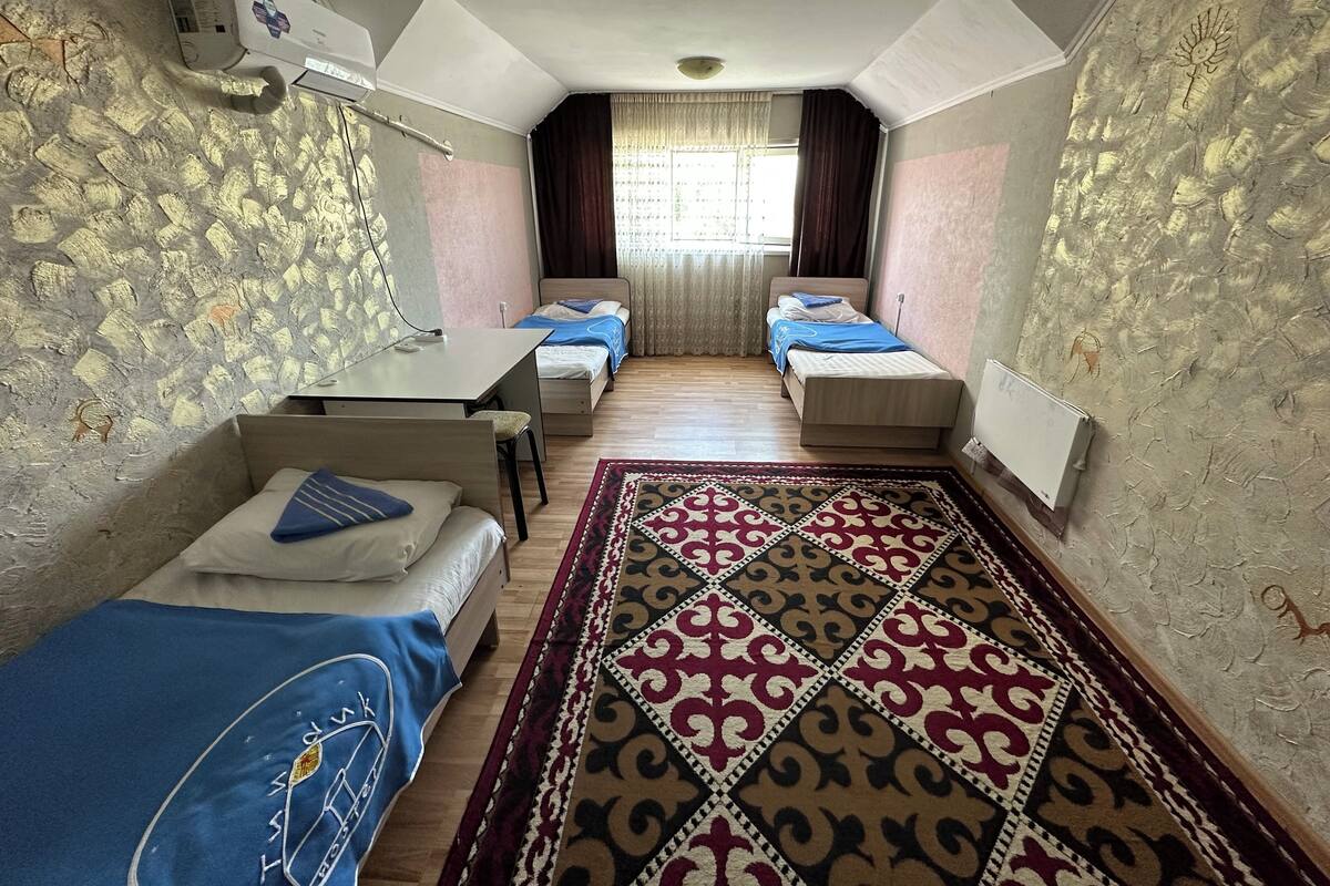 Ein kleines Zimmer mit zwei Einzelbetten, einem kleinen Tisch und einem Fenster mit Vorhängen.