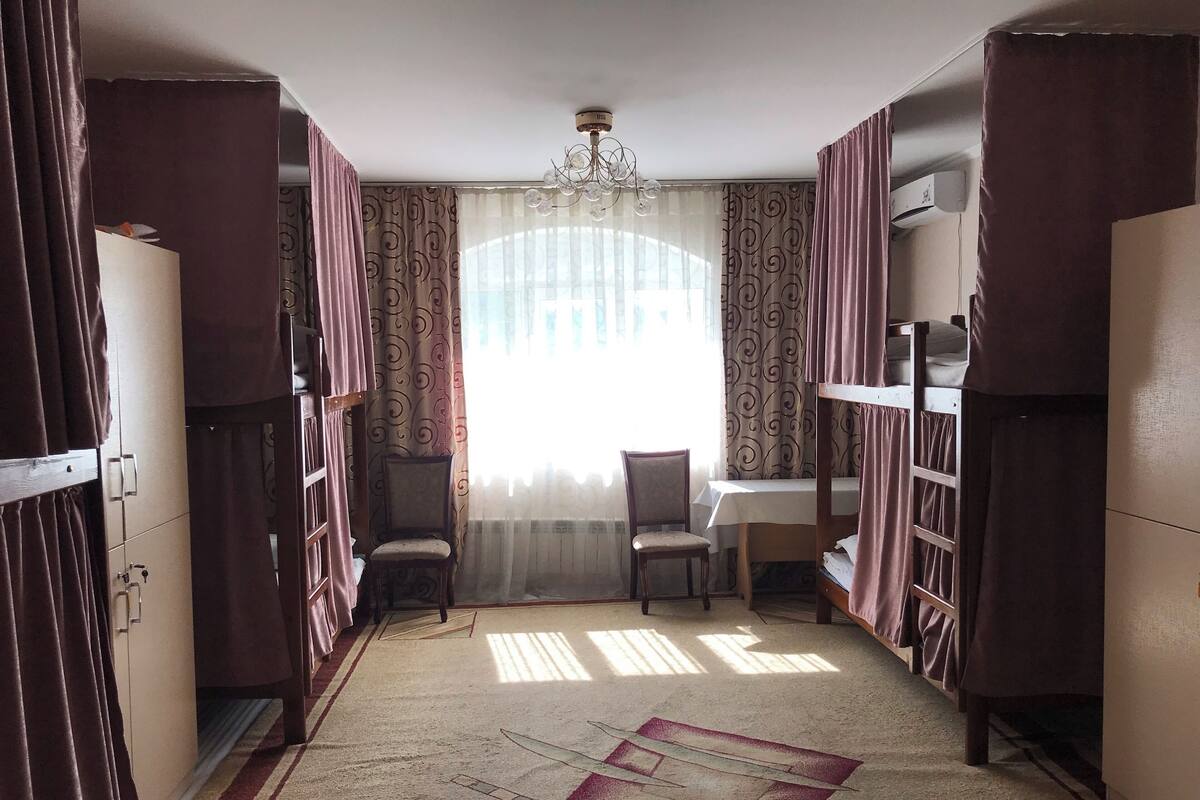 Ein Zimmer mit einem Bett, einem Schreibtisch und einem Stuhl. Es gibt ein Fenster mit Vorhängen, eine Chandelier und eine Klimaanlage.