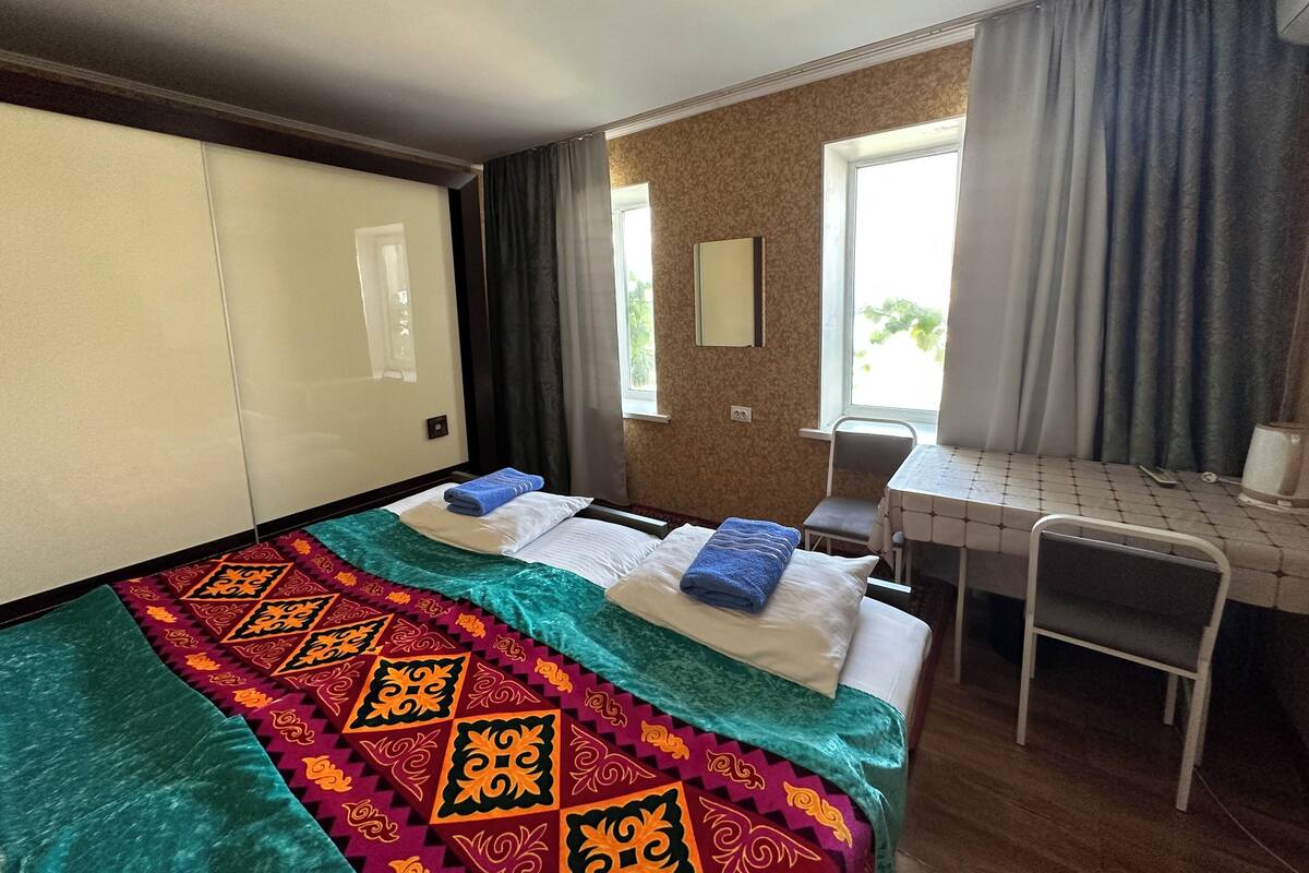 Ein Hotelzimmer mit Bett, Schreibtisch, Stuhl und einem fenster mit Vorhängen.