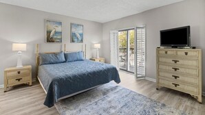 Een slaapkamer met een bed, een dressoir, een televisie en een openslaande deur naar een balkon.
