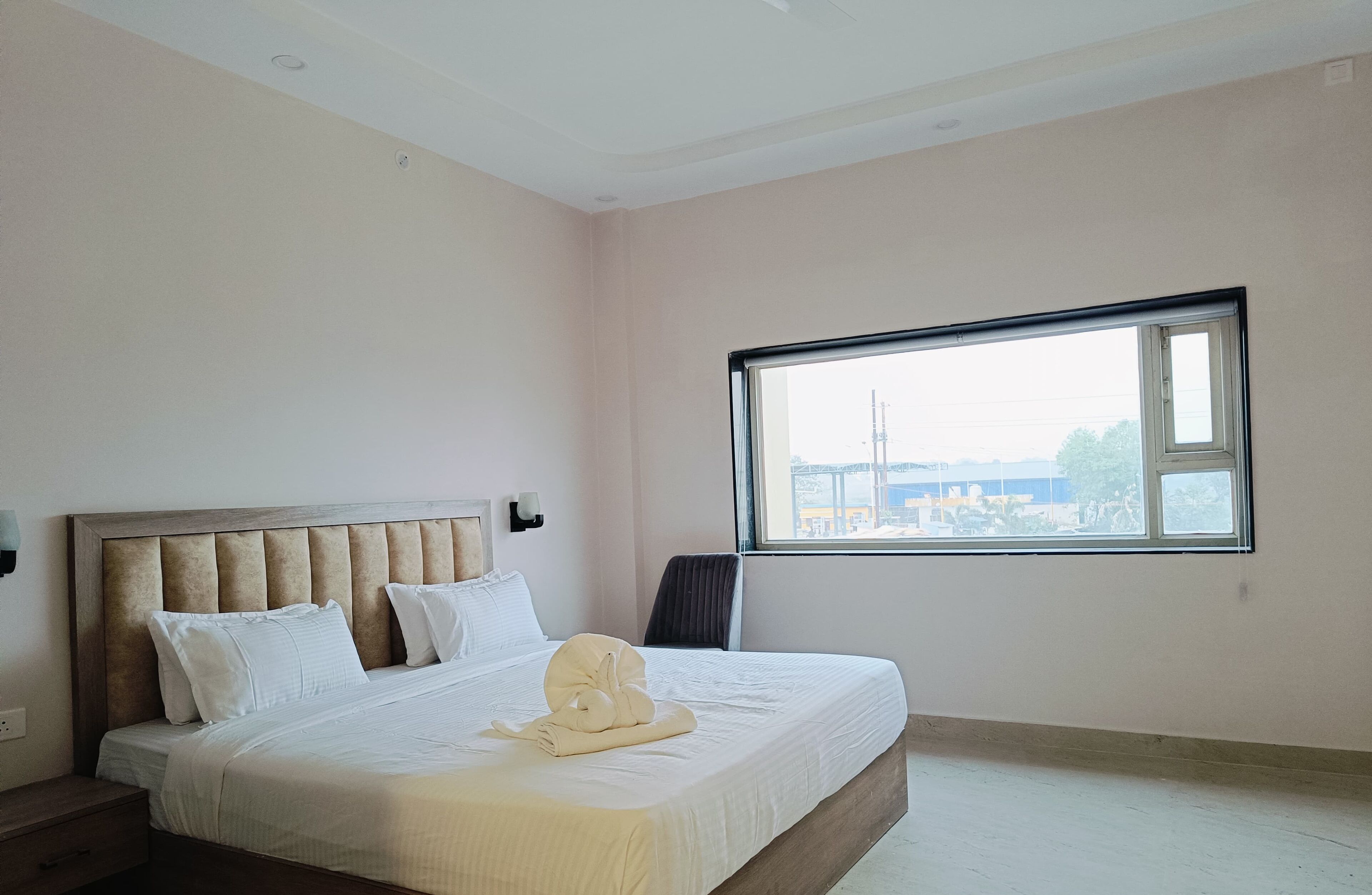 A hotel room with a large bed, a window with a view of the city, and a nightstand.
