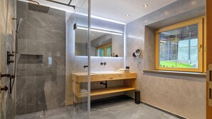 Een moderne badkamer met een douchecabine van glas, een houten wastafelmeubel en een grote spiegel.