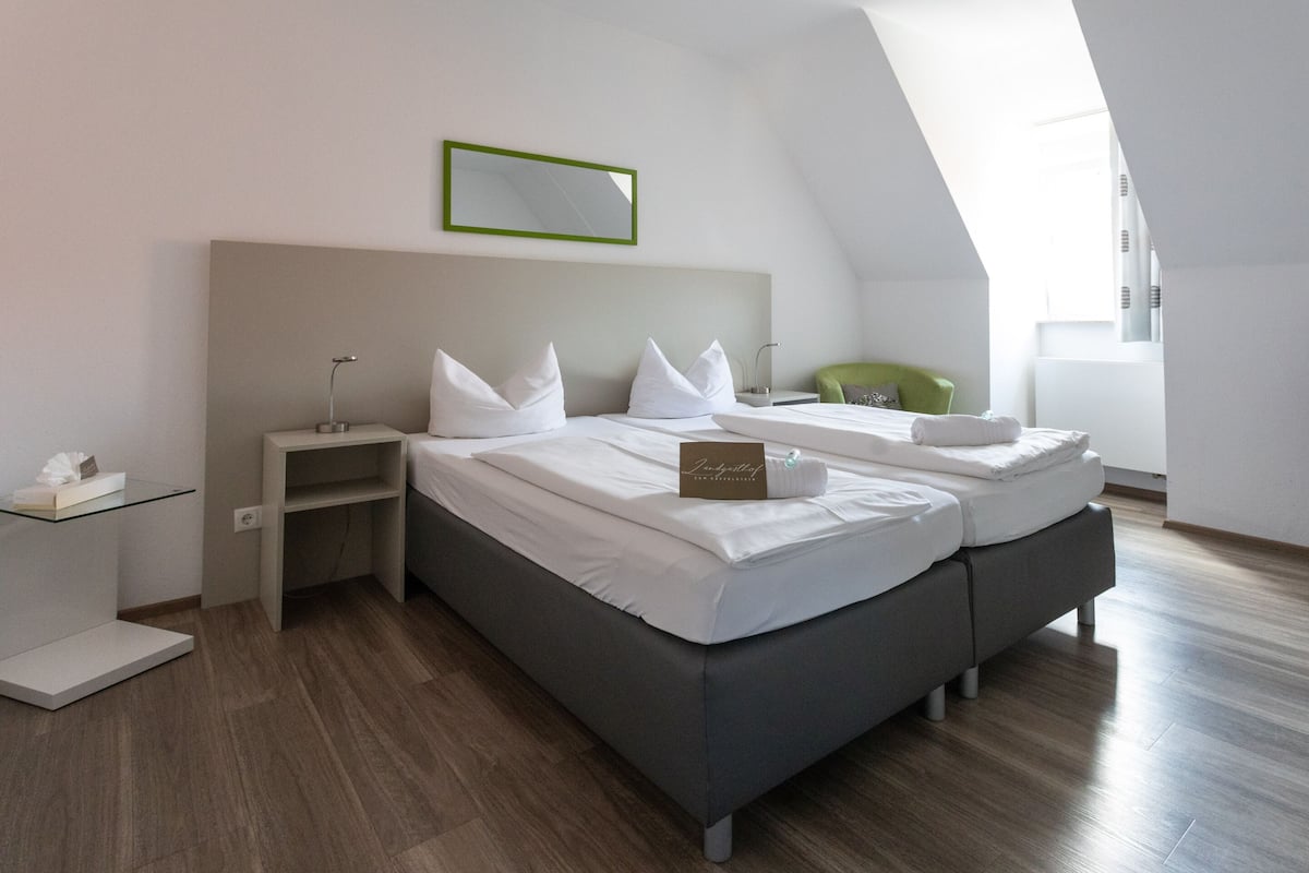 Ein modernes Hotelzimmer mit einem großen Bett, einem Nachttisch, einem grünen Sessel und einem Dachfenster.