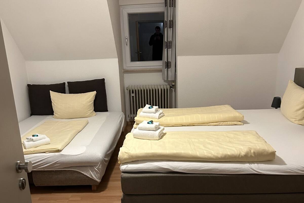 Ein Zimmer mit zwei Betten, jeweils mit Kopfteil, einem Fenster und einer Heizung.