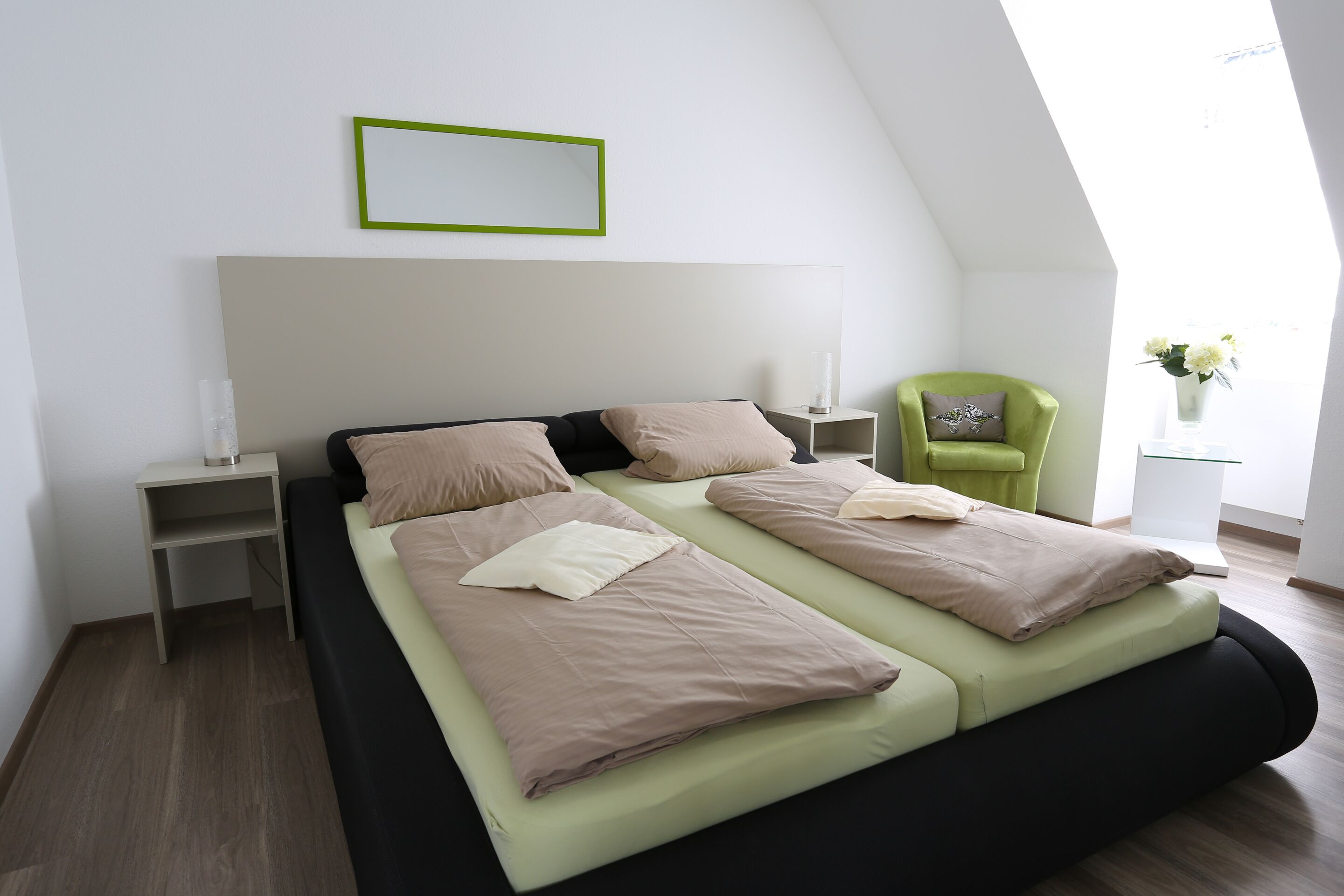 A modern bedroom with a large bed, a green chair, and a bedside table with a lamp.