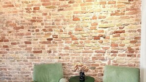 A room with a brick wall and two green armchairs facing each other. - Suite 2 (Ravenna)