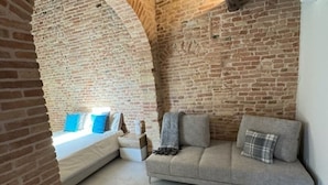 A cozy room with a brick wall, a sofa, and a bed with blue pillows.