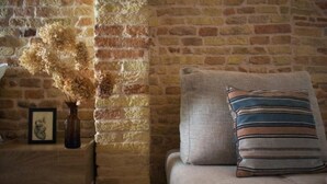 A cozy room with a brick wall, a wooden nightstand with a vase of dried flowers, and a cushioned chair with a striped pillow.