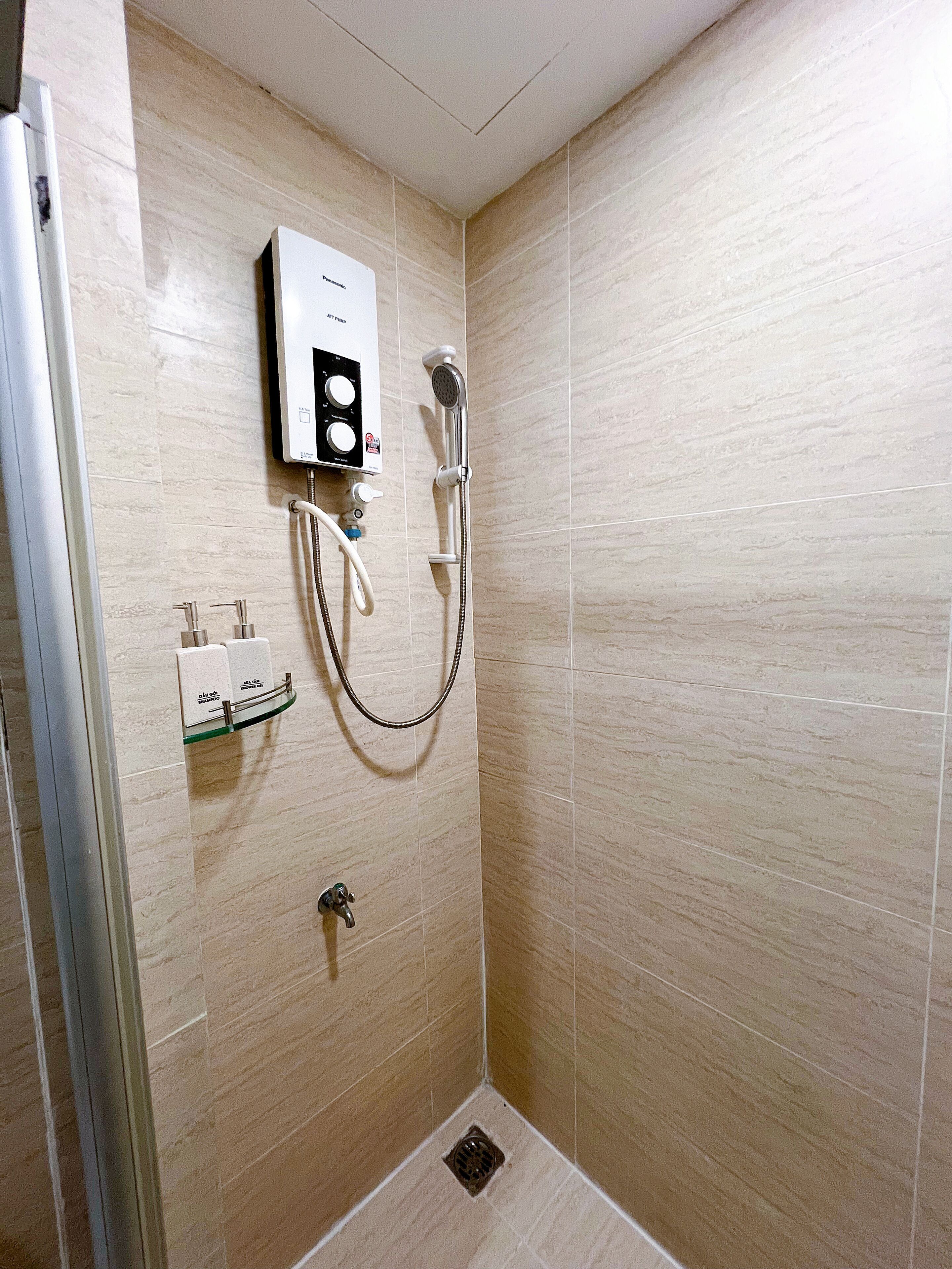 A shower area with a handheld showerhead, a wall-mounted control panel, and a handheld faucet.