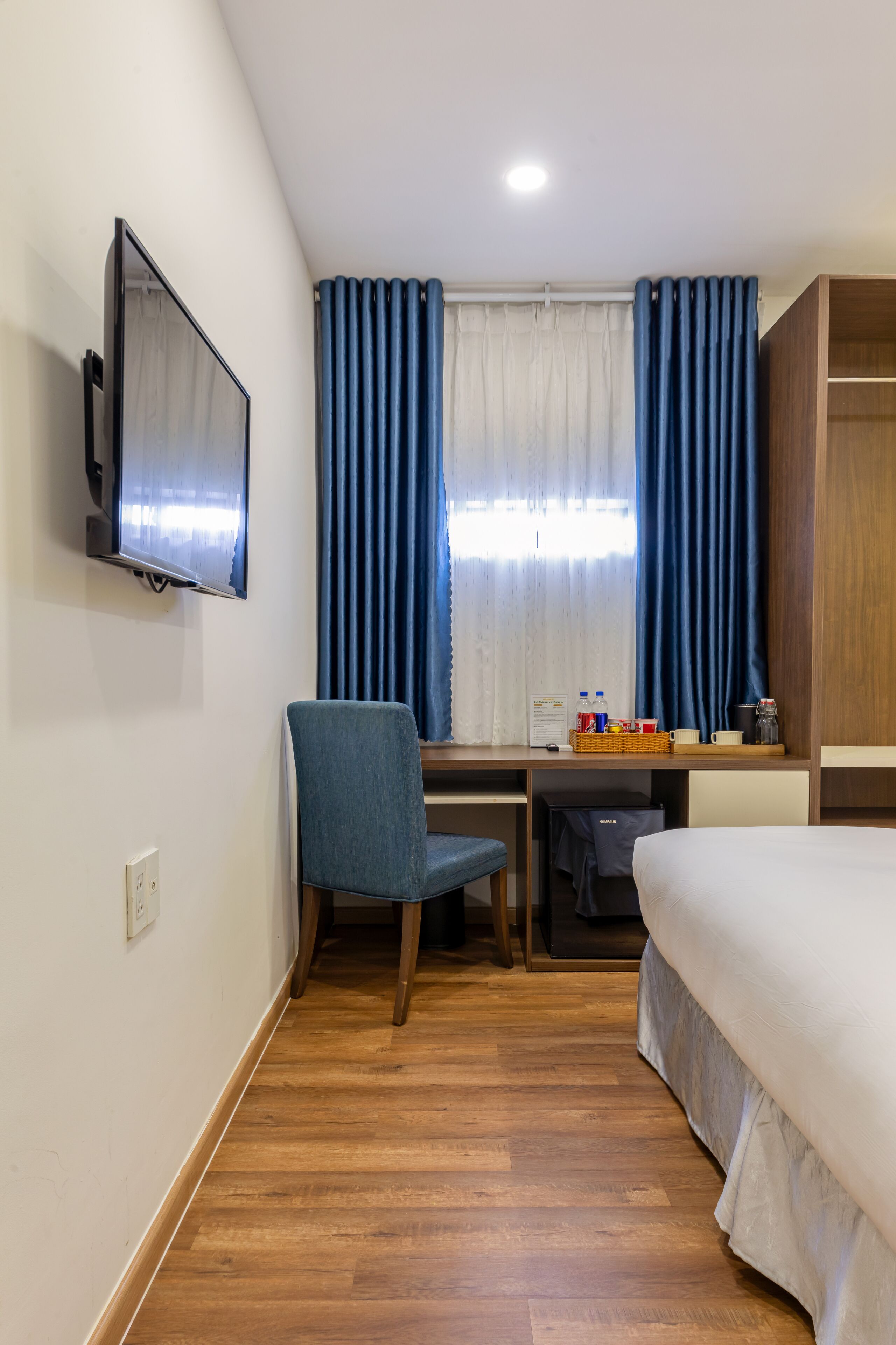 A hotel room with a bed, a desk with a chair, a television, and a window with curtains.