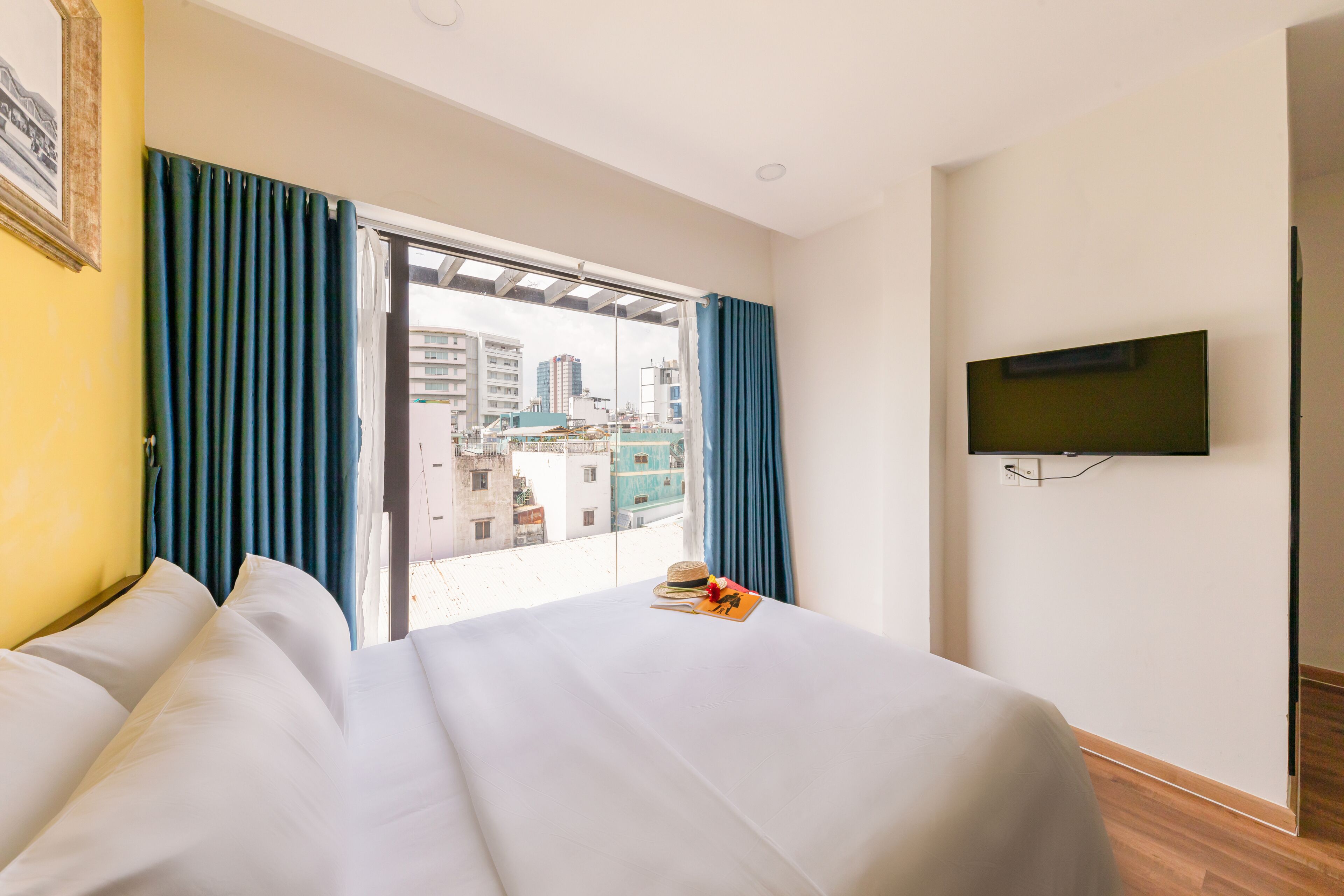 Une chambre d’hôtel avec un lit, un téléviseur fixé au mur et une vue sur la ville par une grande fenêtre.