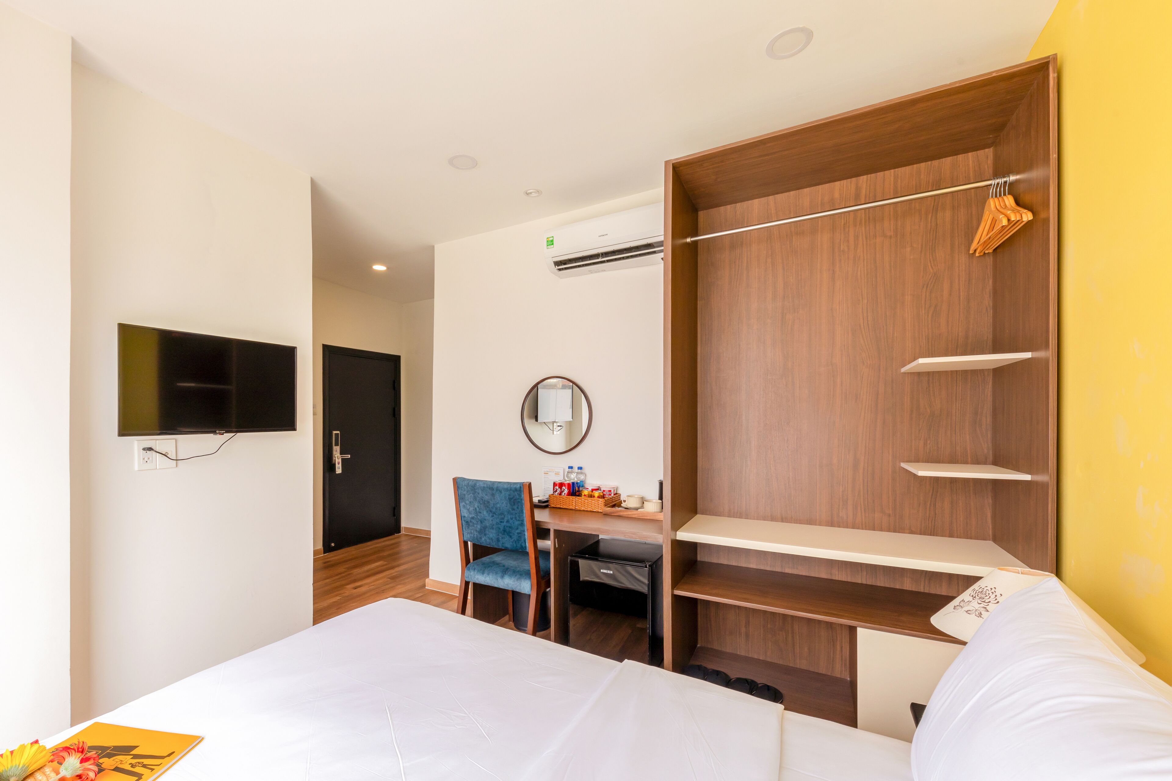 A hotel room with a bed, a desk, a chair, a TV, a wardrobe, and a mirror.