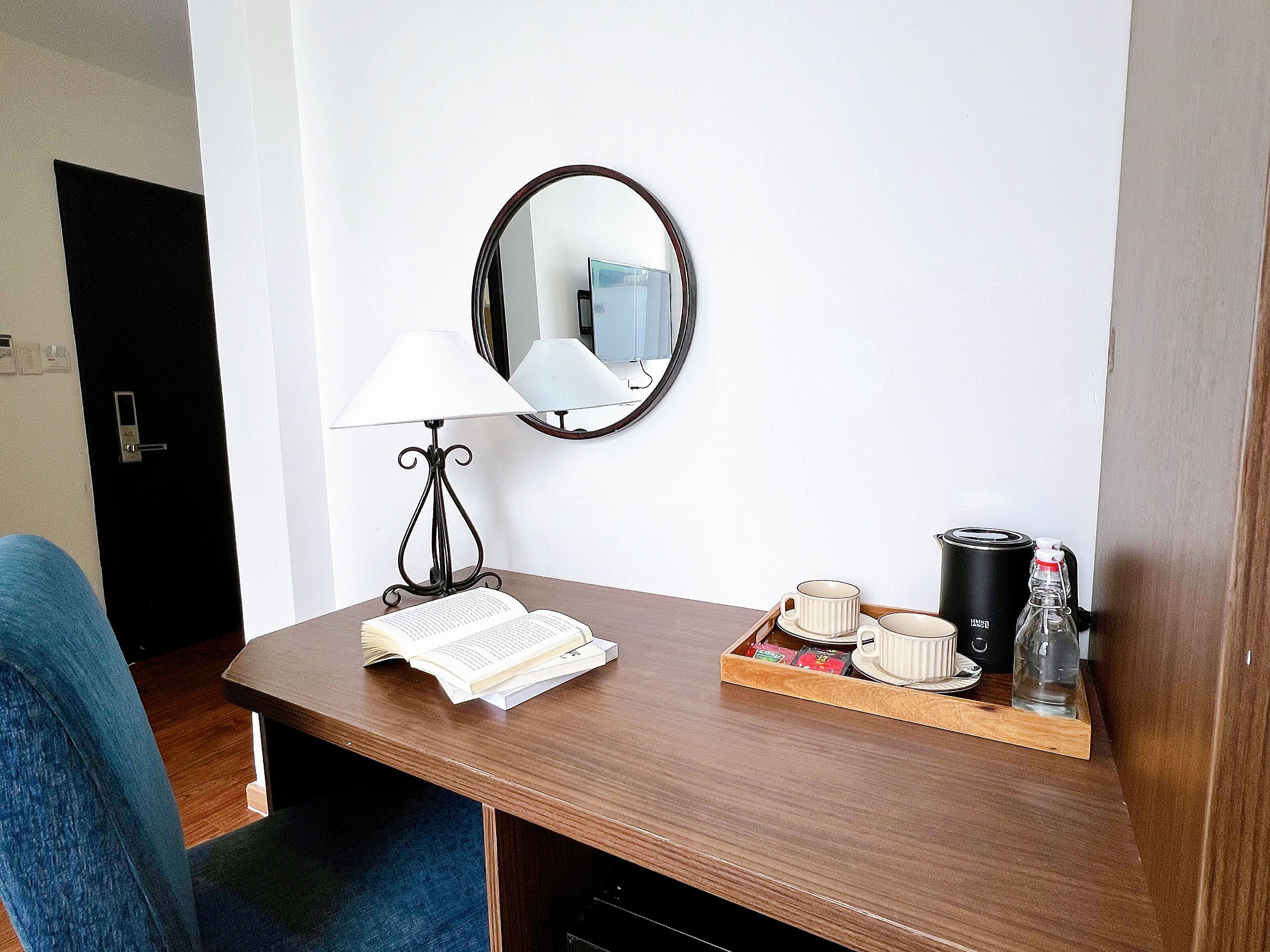 Een houten bureau met een lamp, een spiegel en een dienblad met een boek, mok en koffiezetapparaat.
