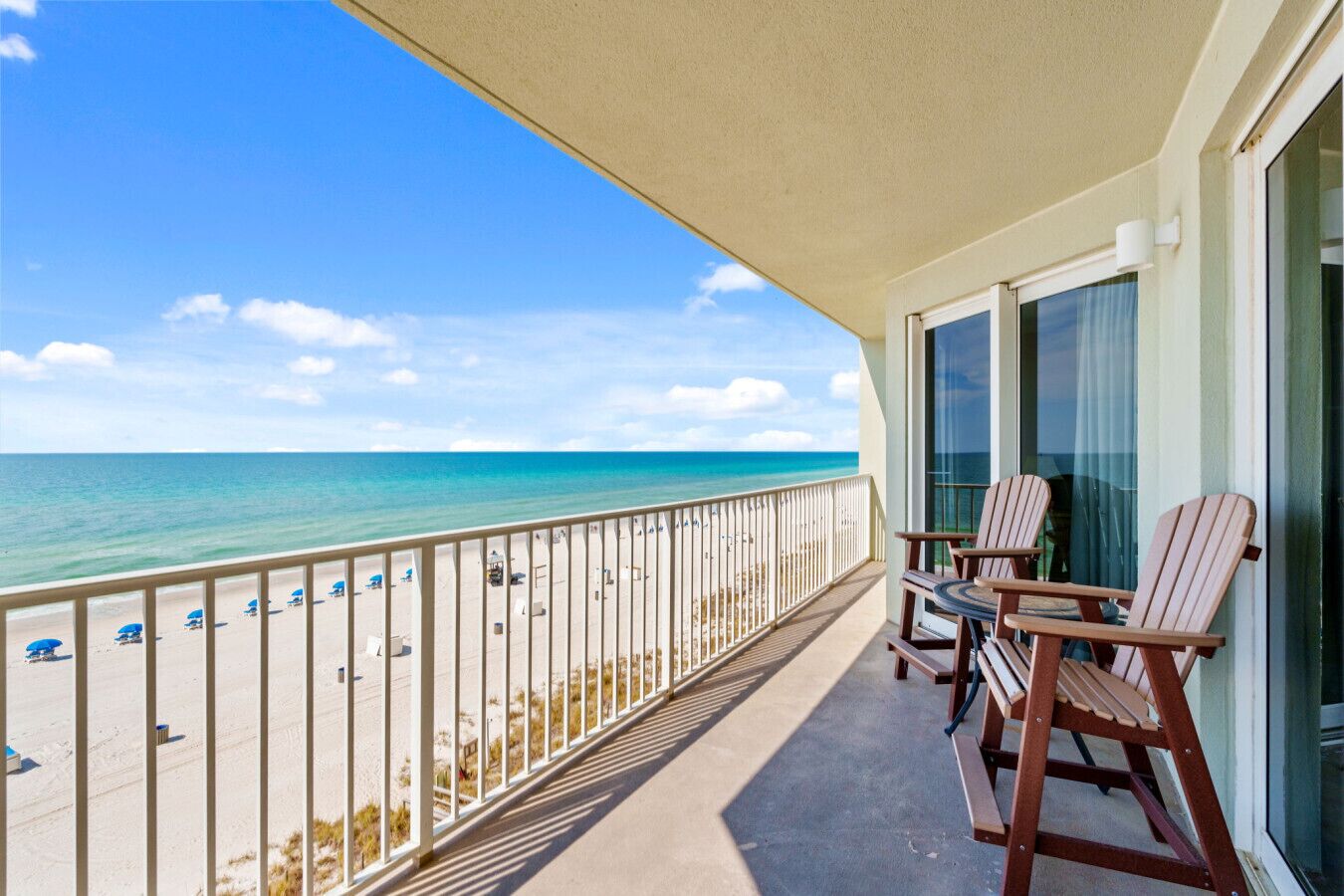 Un balcon avec vue sur la plage et l’océan. On y trouve deux chaises en bois et une table.