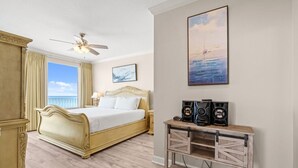 Une chambre à coucher avec un grand lit, un ventilateur de plafond, une commode en bois et un tableau accroché au mur.