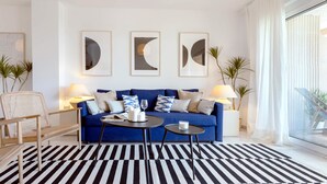 A modern living room with a blue sofa, two side tables, a black and white striped rug, and three framed abstract wall art pieces. - Genteel Home Ricardo Soriano III (Marbella)