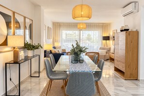A modern living room with a glass dining table, grey upholstered chairs, a wooden cabinet, and a large window with curtains. - Genteel Home Ricardo Soriano III (Marbella)