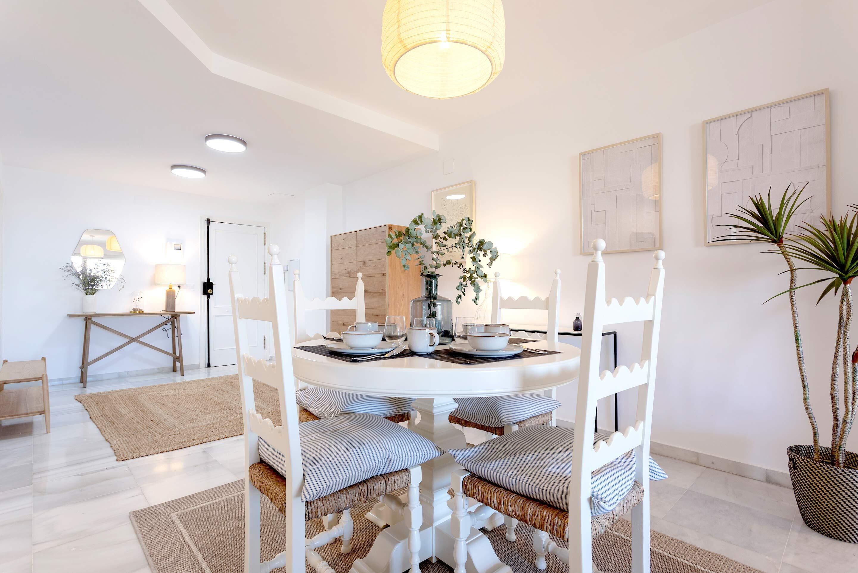 A dining area with a round table, white chairs, and a hanging light fixture.