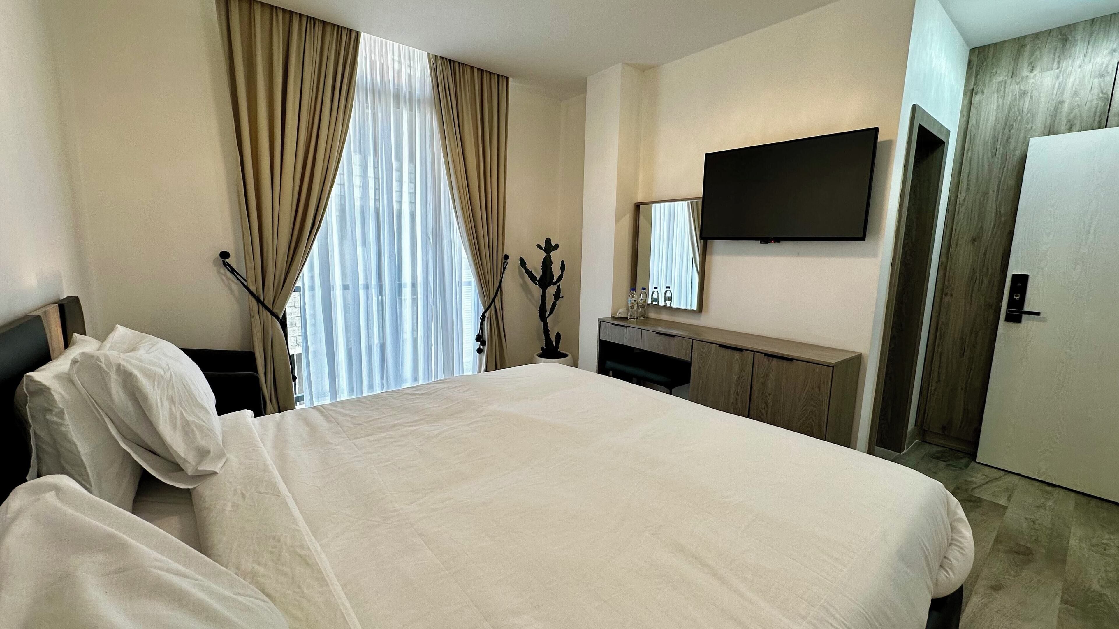 A hotel room with a bed, a TV mounted on the wall, a desk with a mirror, and a door.
