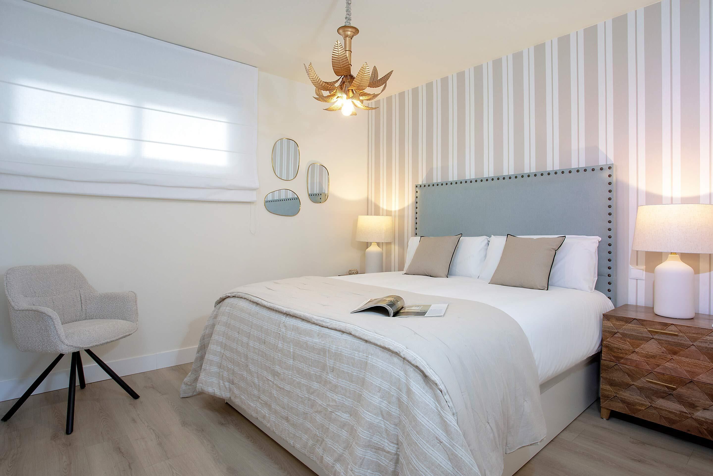 Un dormitorio con cama, lámparas de noche, una silla y un candelabro.