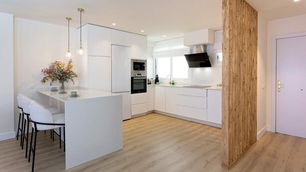 A modern kitchen with white cabinetry, a central island, and a wooden accent wall. - Genteel Home San Pancracio (Fuengirola)