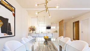 A modern dining area with a glass table, white chairs, a gold bowl centerpiece, and a chandelier. - Genteel Home San Pancracio (Fuengirola)