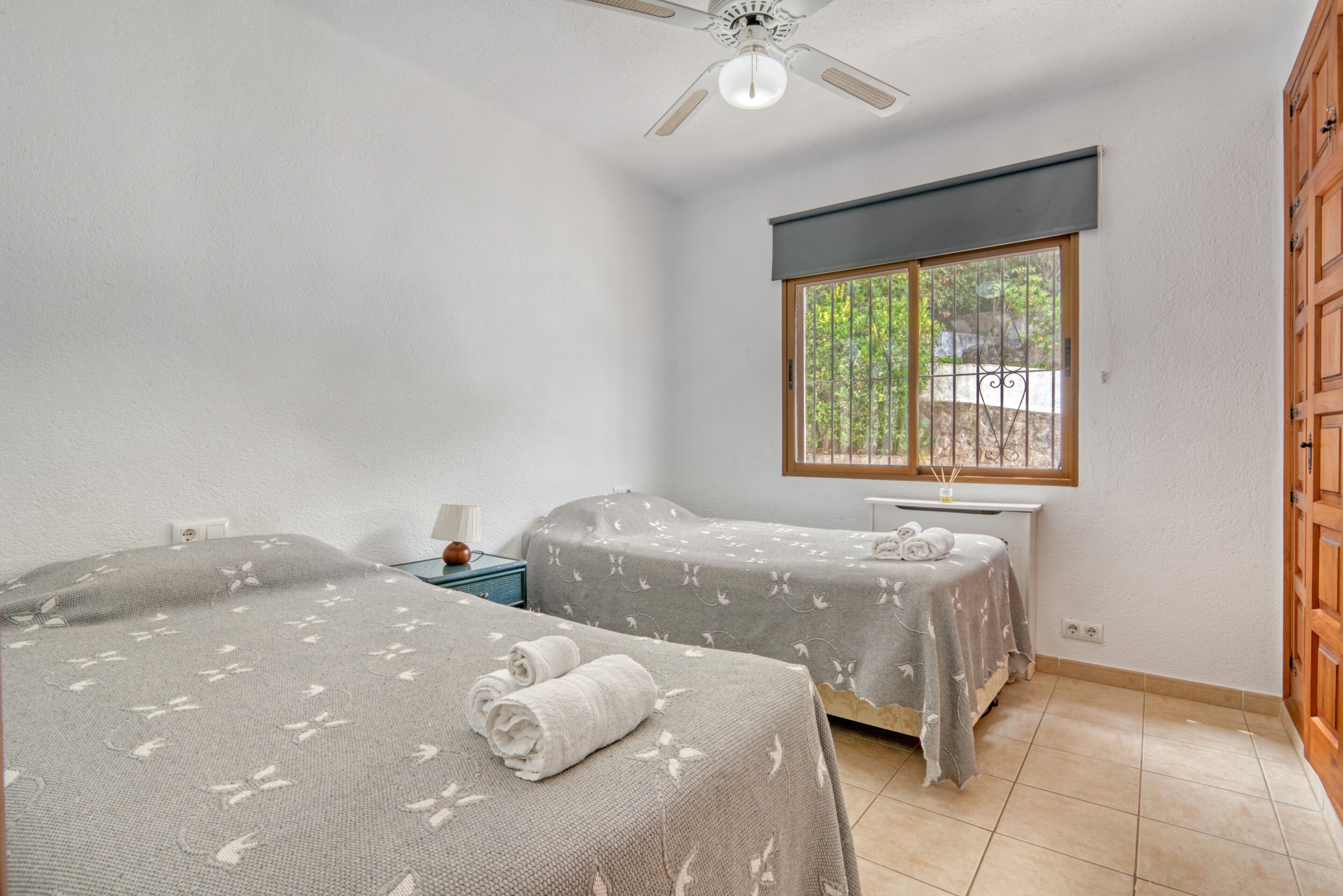 A room with two beds, a window with a view, a ceiling fan, and a wooden wardrobe.