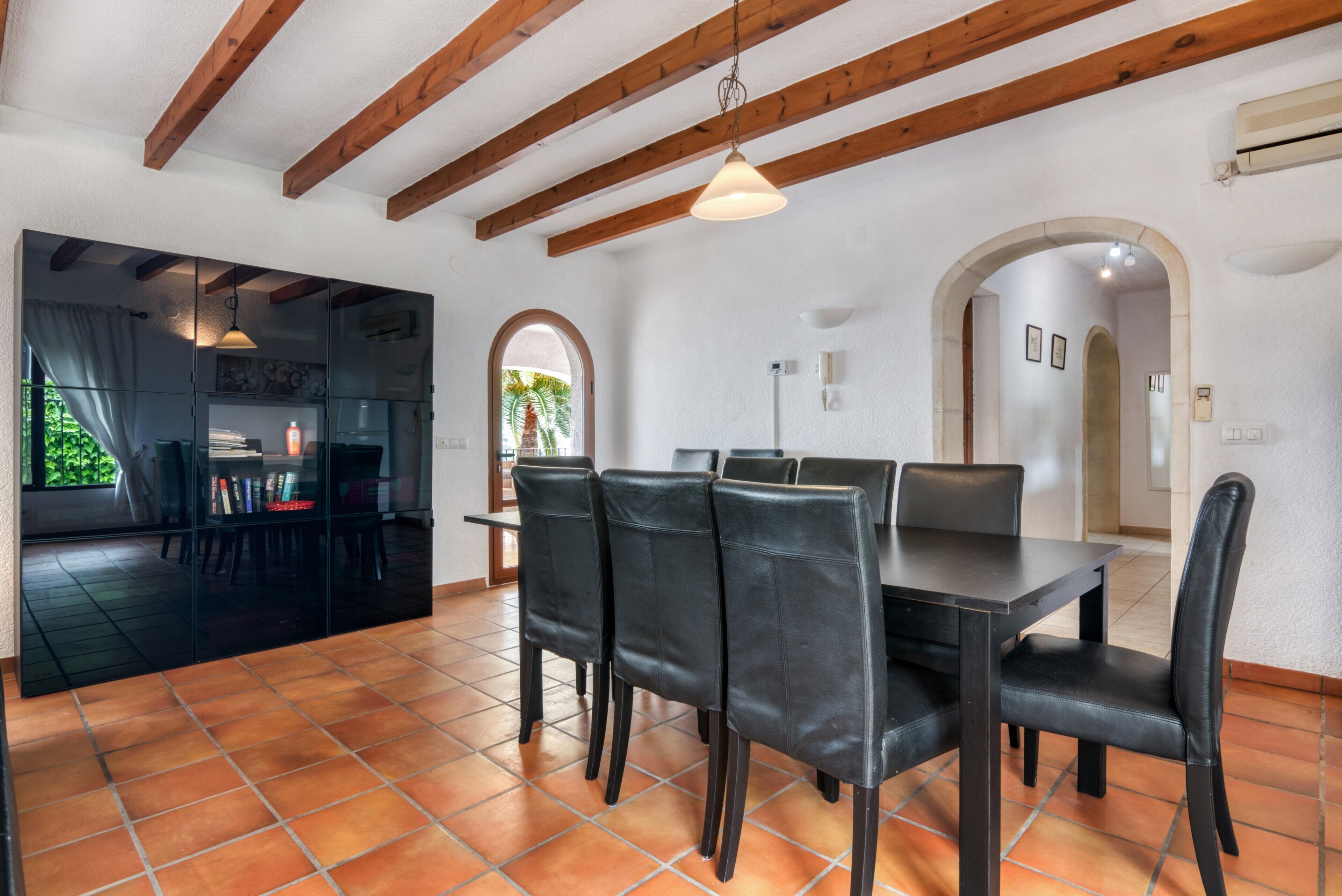 Un espace repas avec une table et des chaises, une cuisine en arrière-plan et une vue à travers une arche.