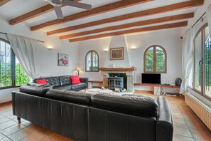 A living room with a black leather sofa, a fireplace, and large windows. - Villa 'Casa Ann - Family Rentals' with Sea View, Private Pool and Wi-Fi (Jávea)