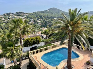 A pool surrounded by palm trees and a view of a hillside town. - Villa 'Casa Ann - Family Rentals' with Sea View, Private Pool and Wi-Fi (Jávea)