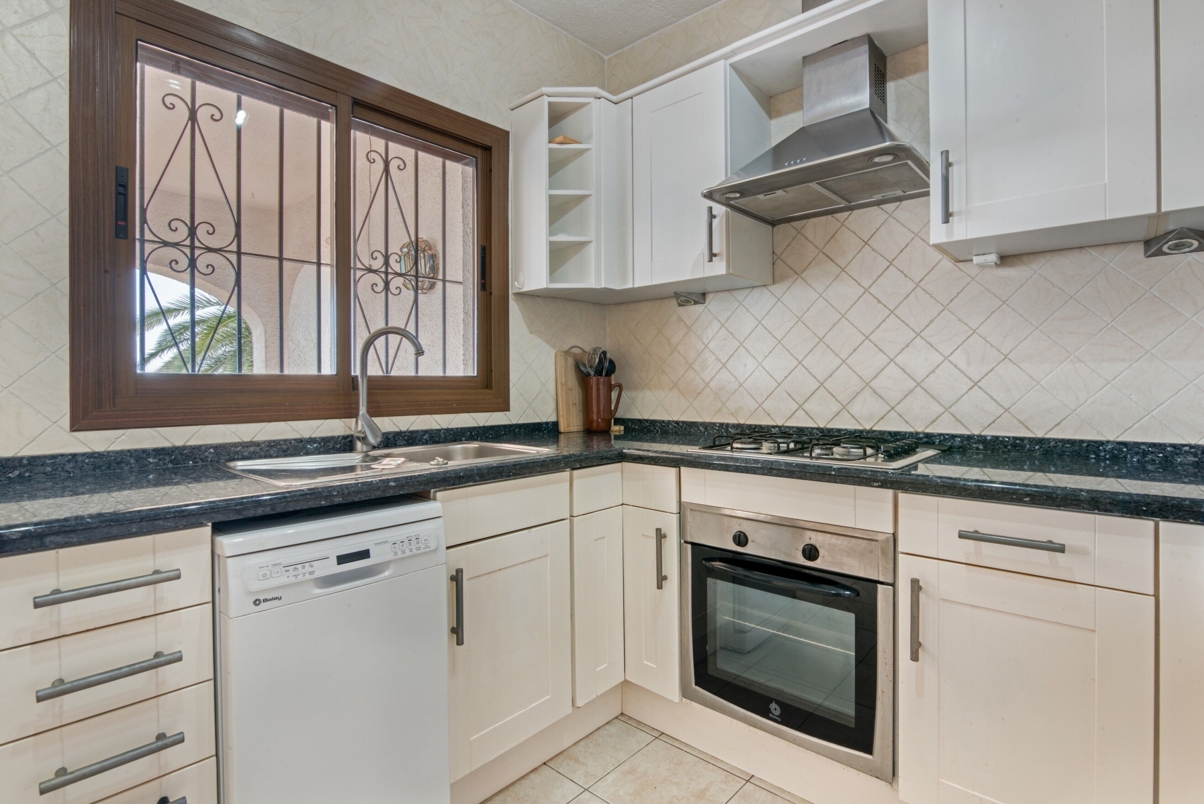 A kitchen with a dishwasher, oven, and a window with decorative bars.