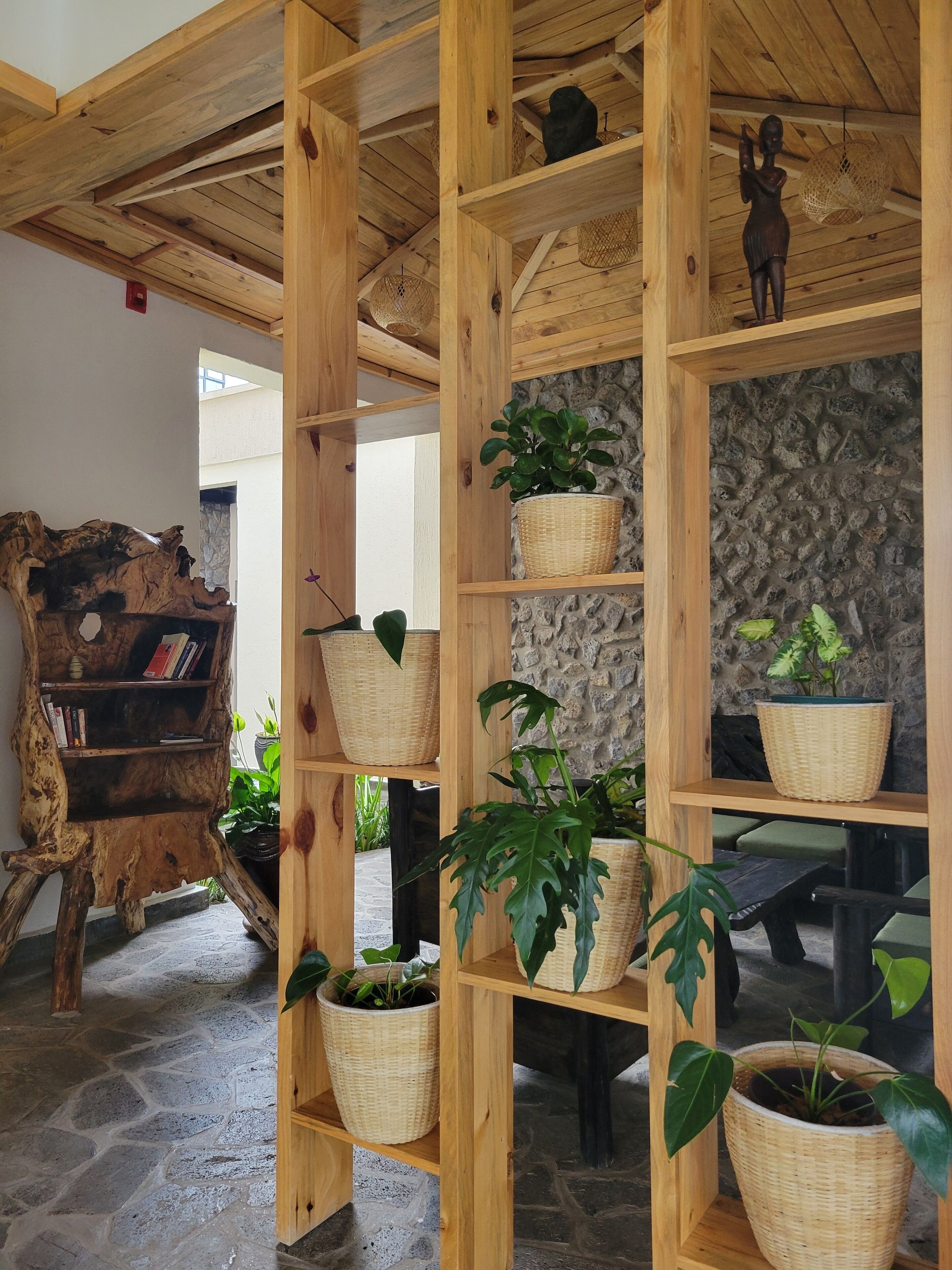 Ein Holzregal mit gewebten Körben, die Pflanzen enthalten, ein rustikales Bücherregal und eine Steinwand im Hintergrund.