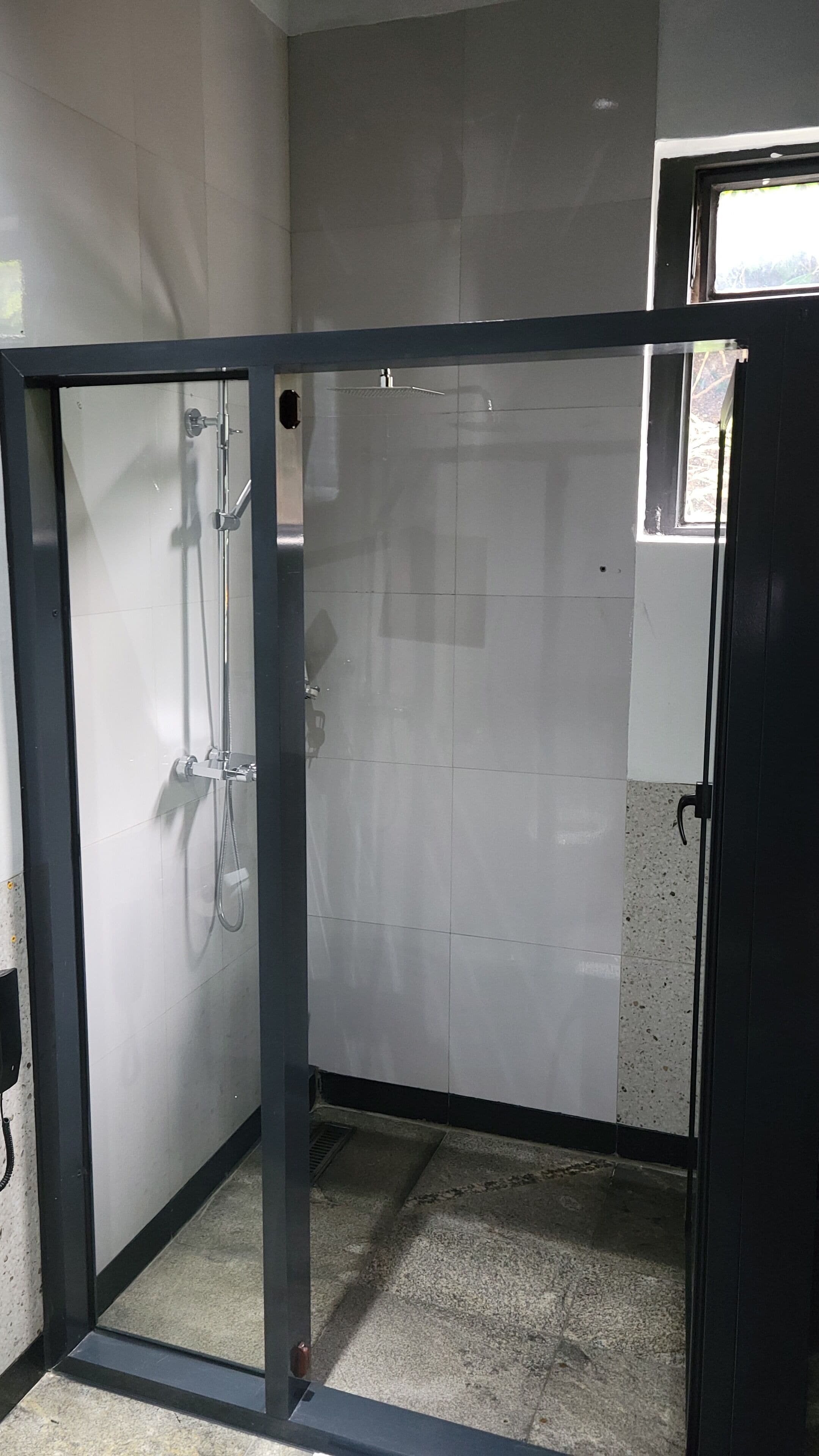 A glass-enclosed shower area with a tiled floor, a visible showerhead, and a door frame.