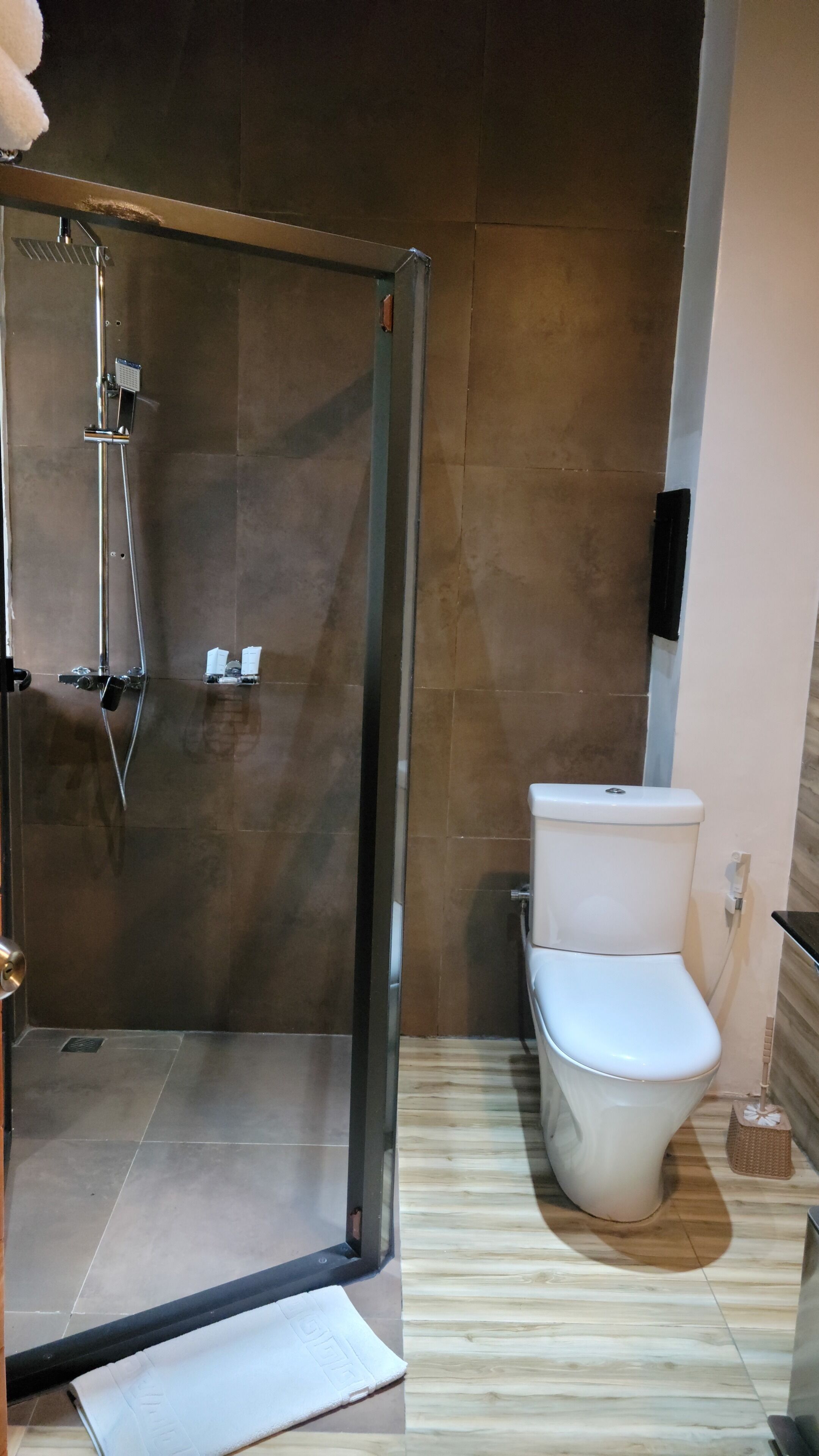 A bathroom with a glass-enclosed shower, a toilet, and a wooden floor.