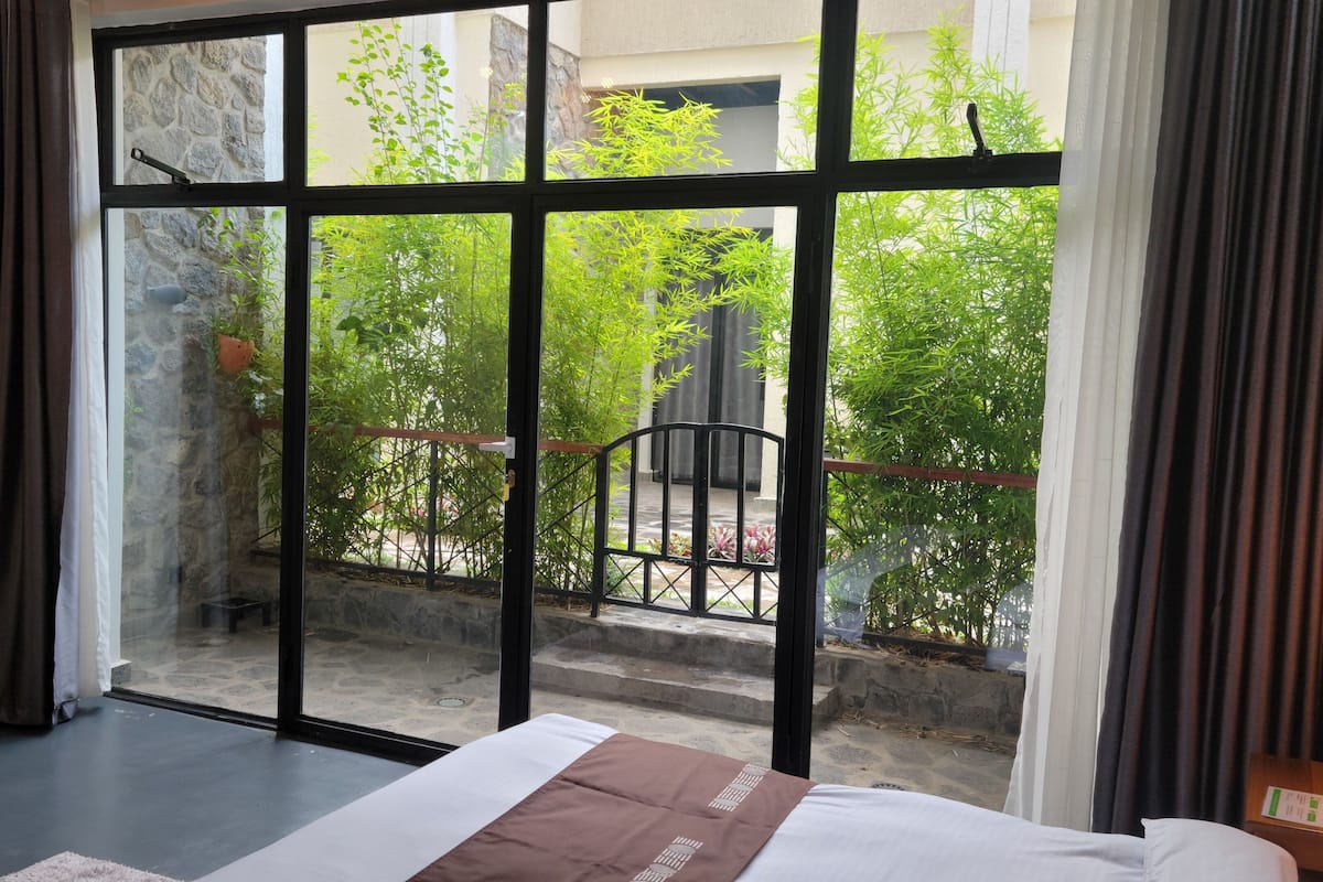 A room with a bed, a large window, and a view of greenery outside.