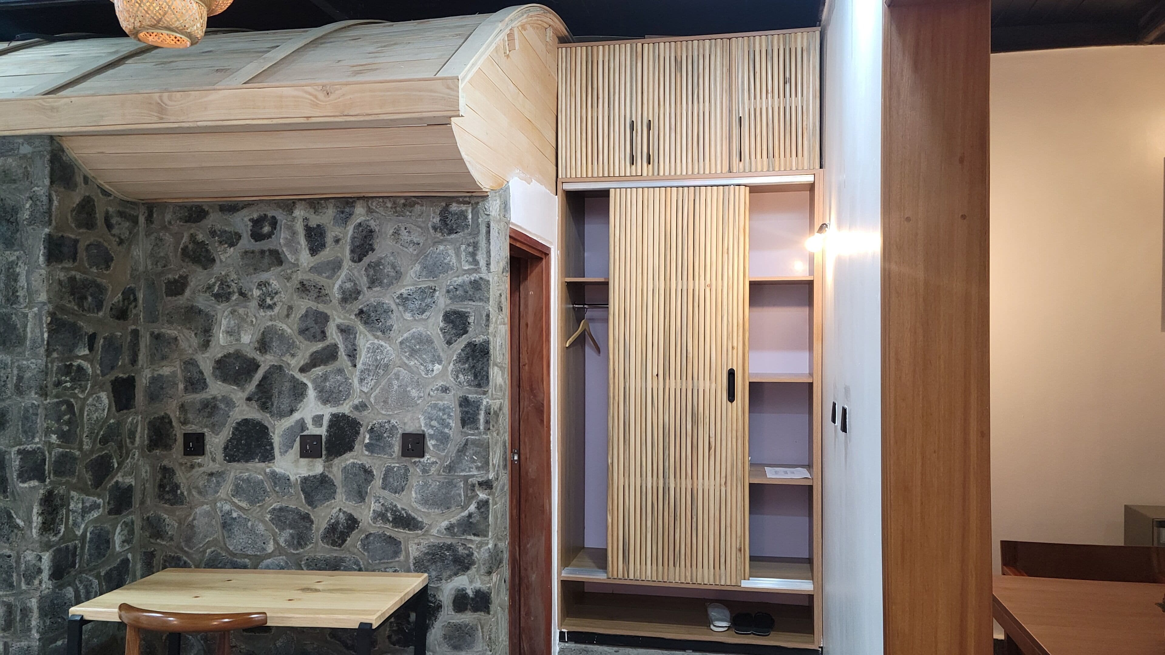 Ein Zimmer mit Steinwand, Holzmöbeln und einem eingebauten Kleiderschrank mit vertikalen Lamellen.