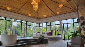 Una habitación amplia con techo alto, ventanas grandes y un área de estar con sofá y sillones.