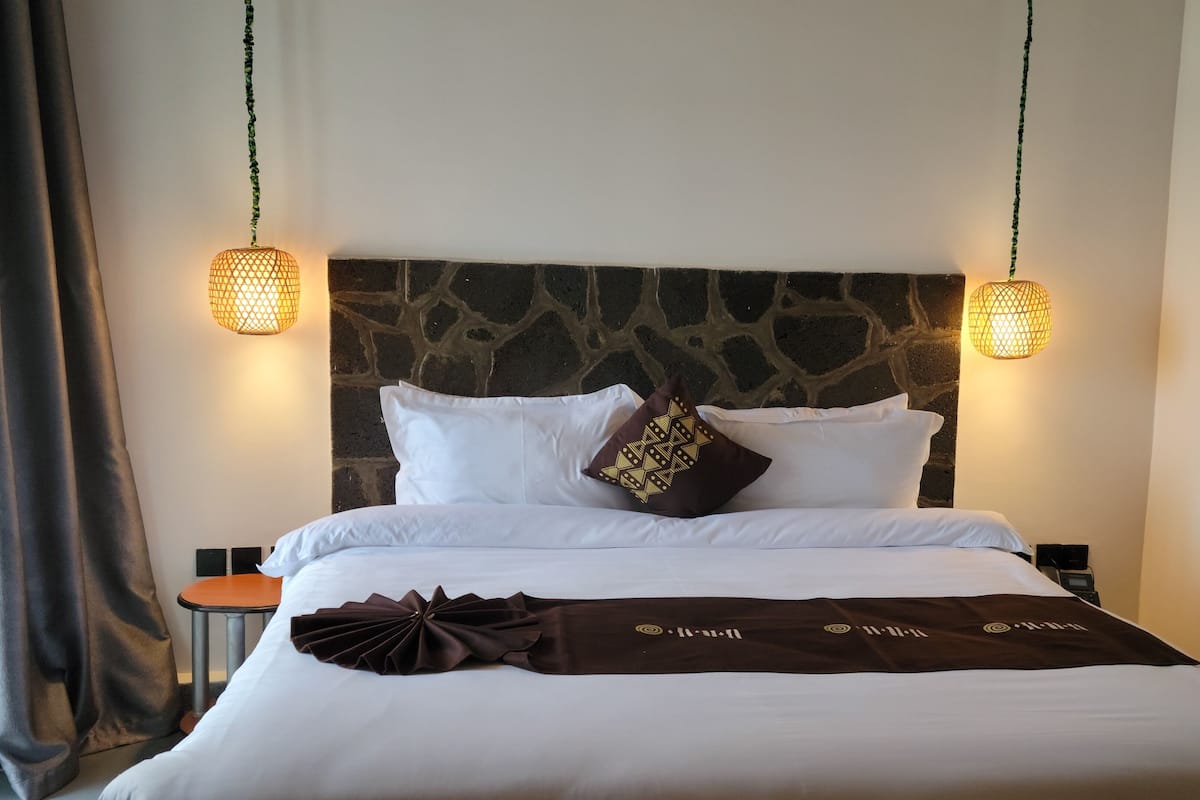 A neatly made bed with white and brown linens, a stone-patterned headboard, and two wall-mounted lamps.