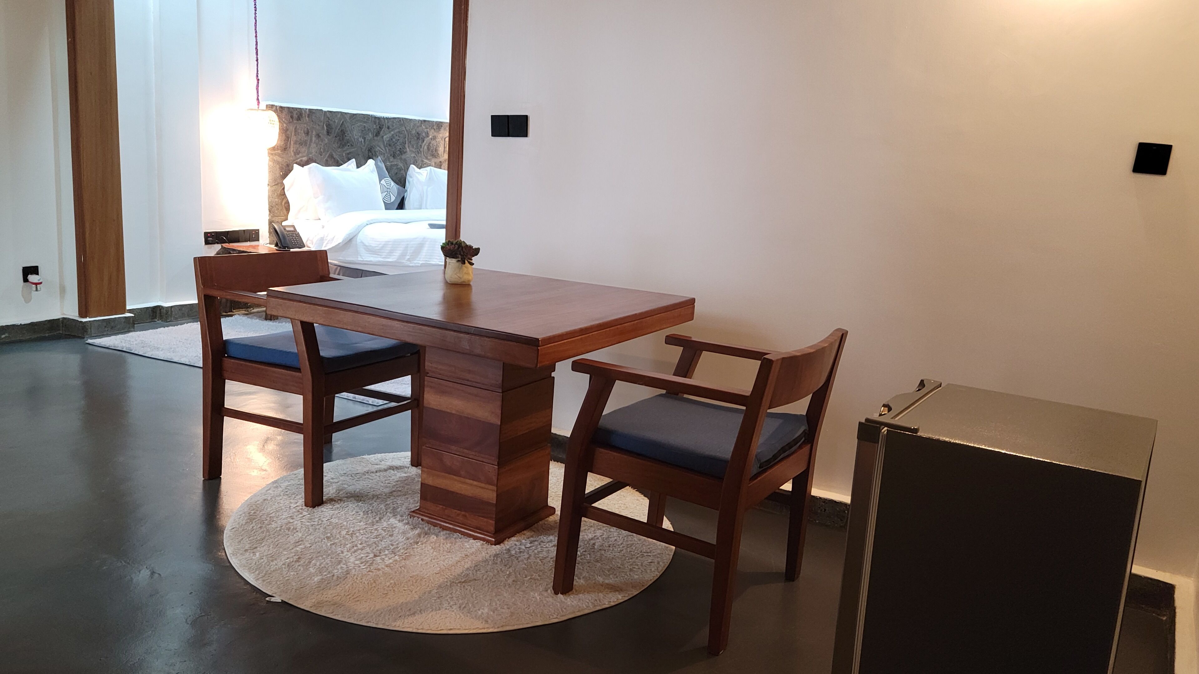 Ein Essbereich mit einem Holztisch, zwei Stühlen, einem kleinen Teppich und einem kompakten Kühlschrank.
