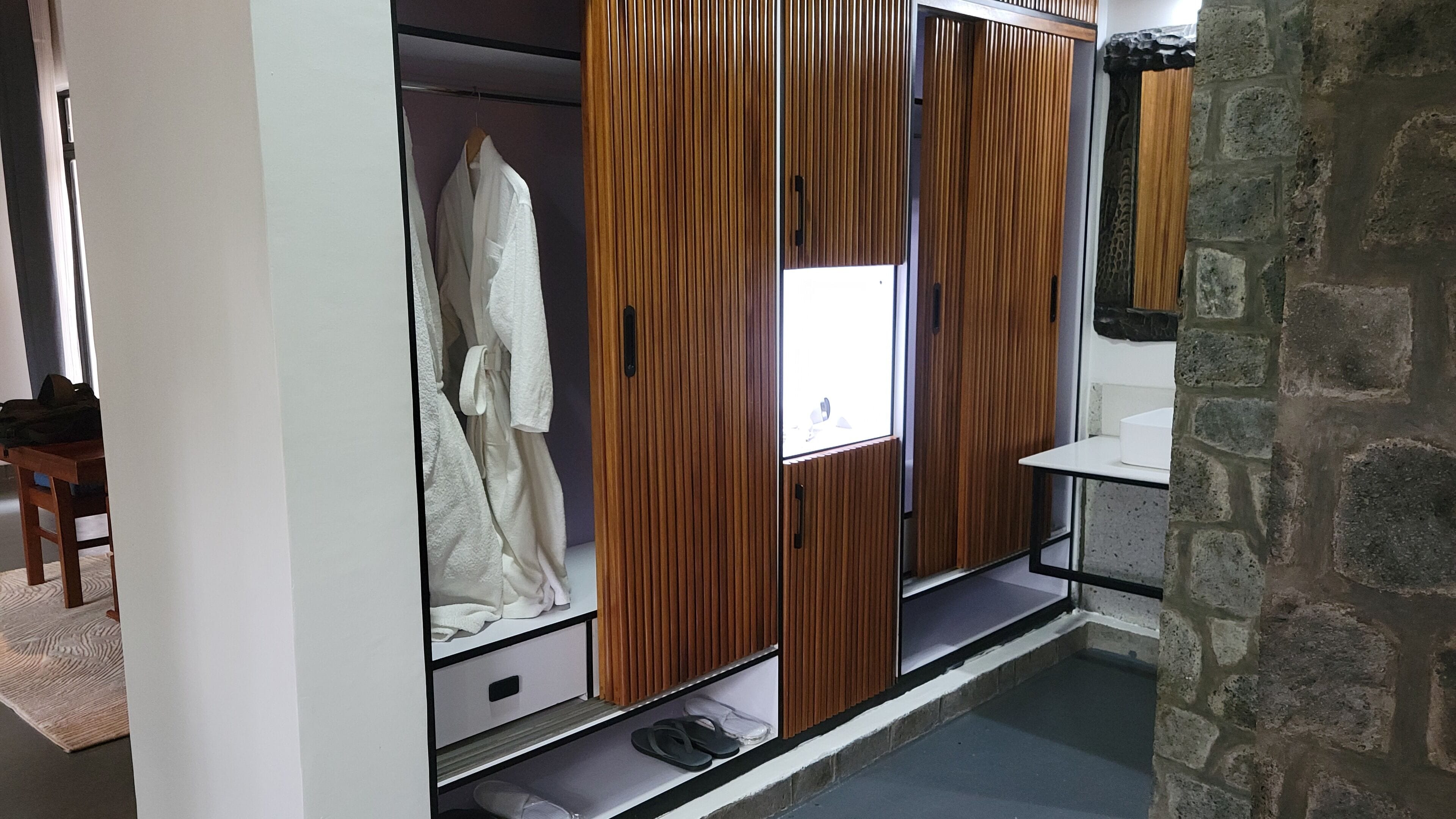 Un dressing avec des portes coulissantes en bois, une robe blanche suspendue et une petite étagère sur laquelle reposent une paire de pantoufles.