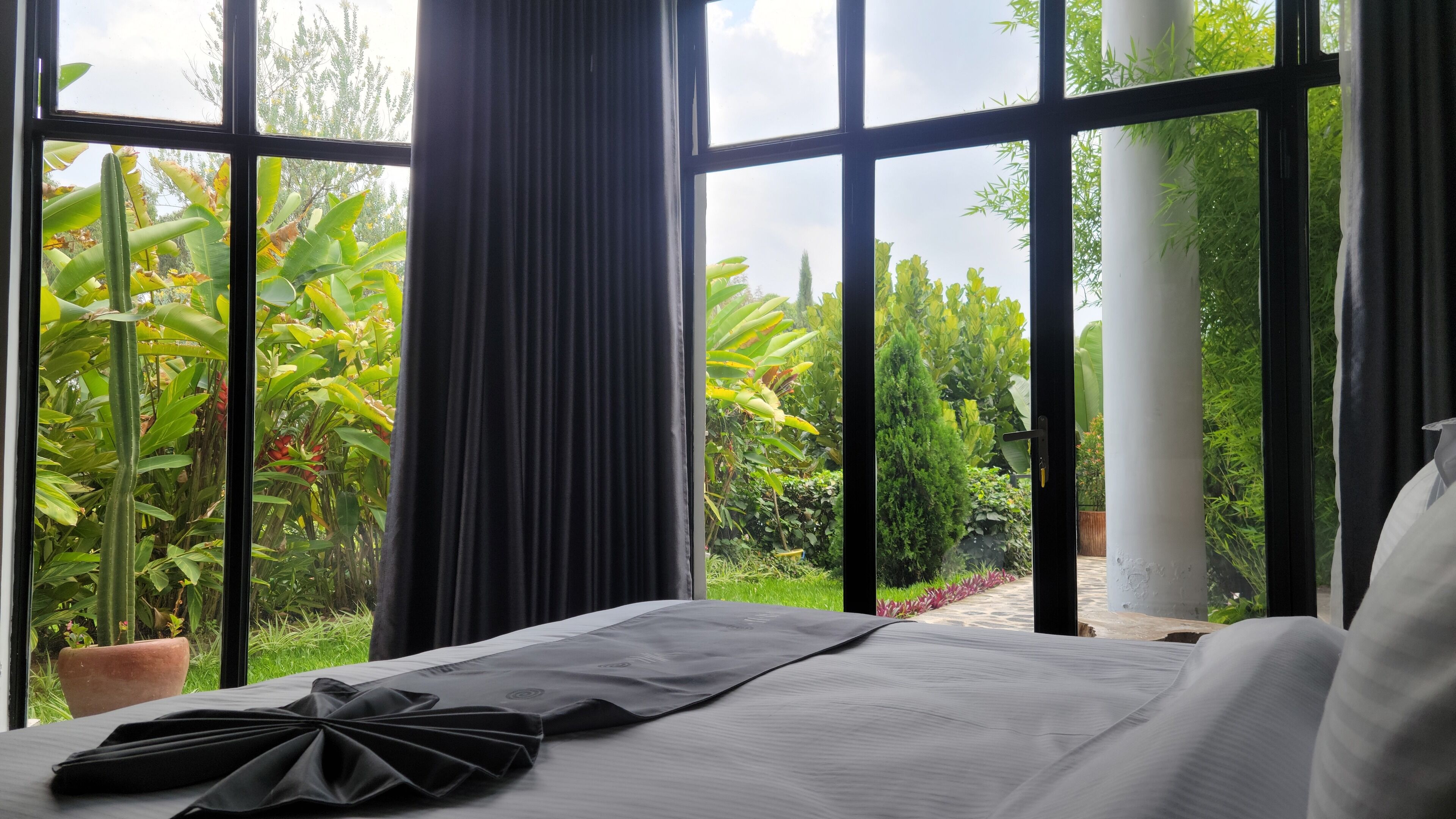 A bedroom with a large window, a bed, and a view of a garden.