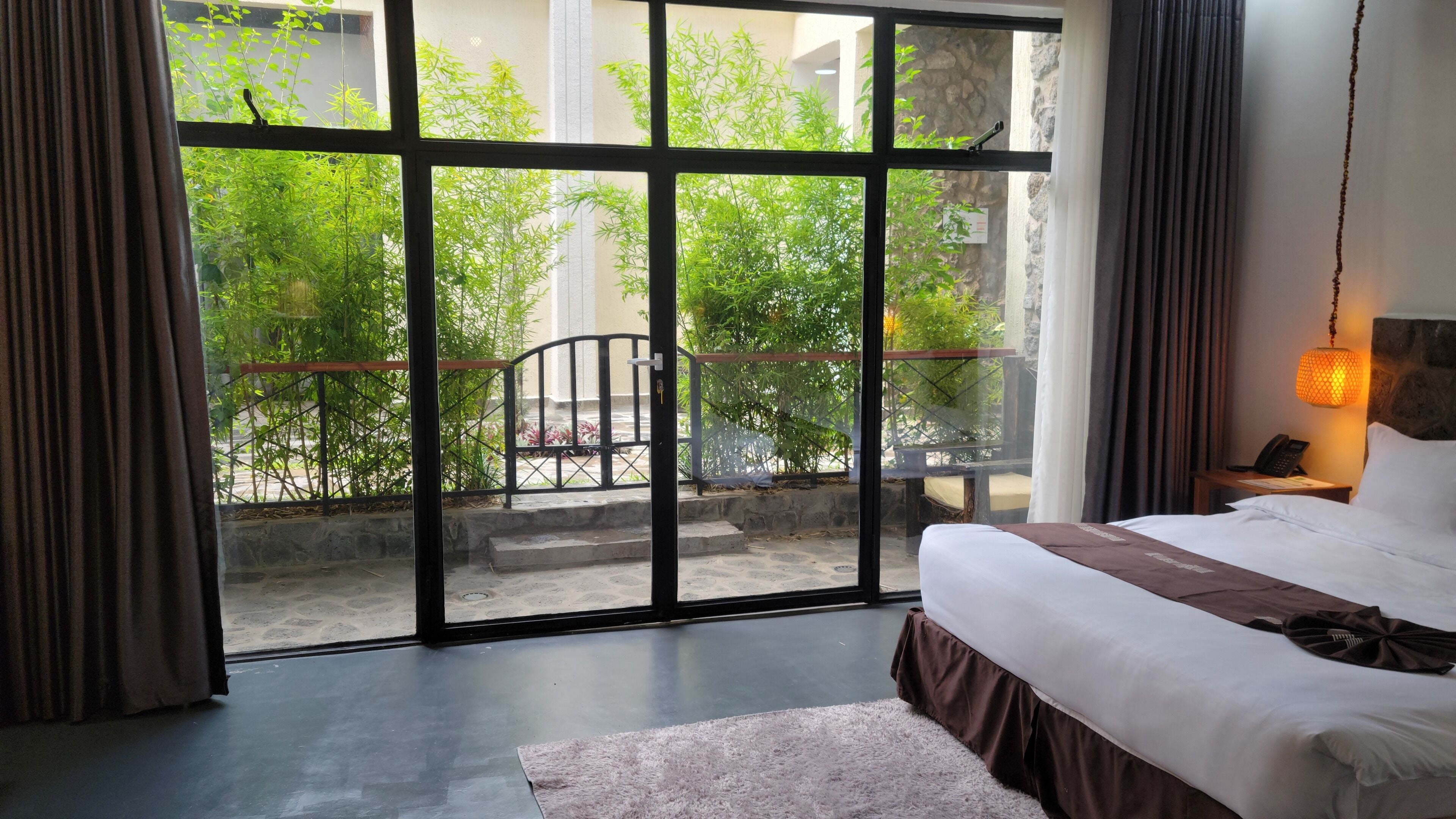 A hotel room with a large sliding glass door leading to an outdoor area with bamboo plants.