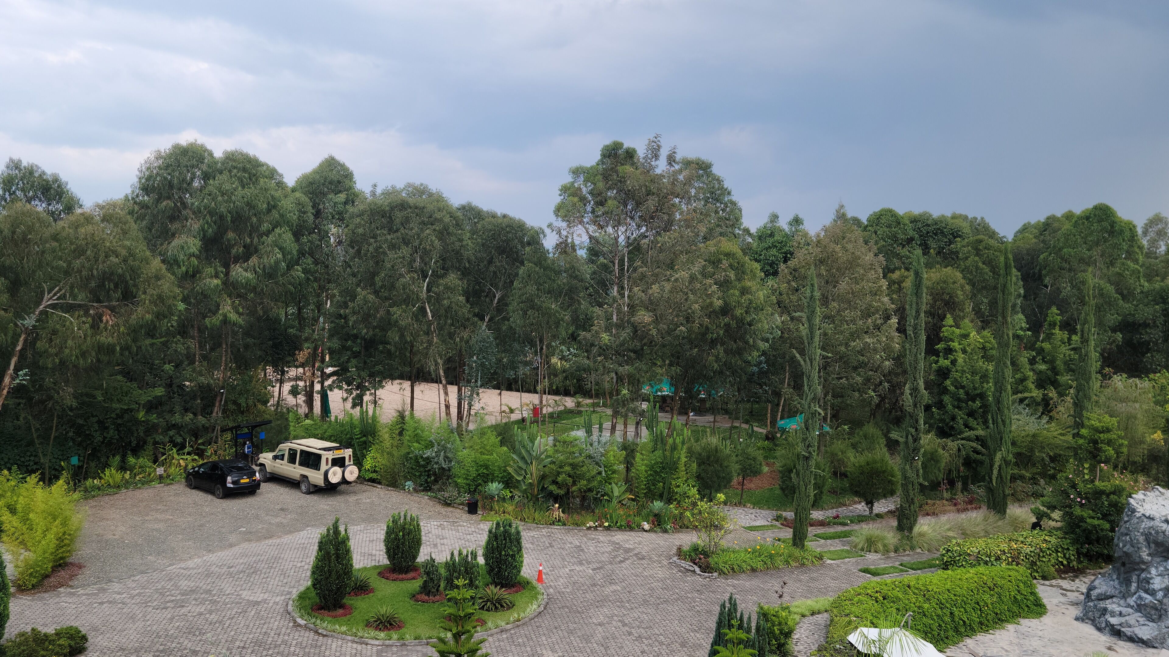 A paved parking area with a few vehicles, surrounded by lush greenery and trees.