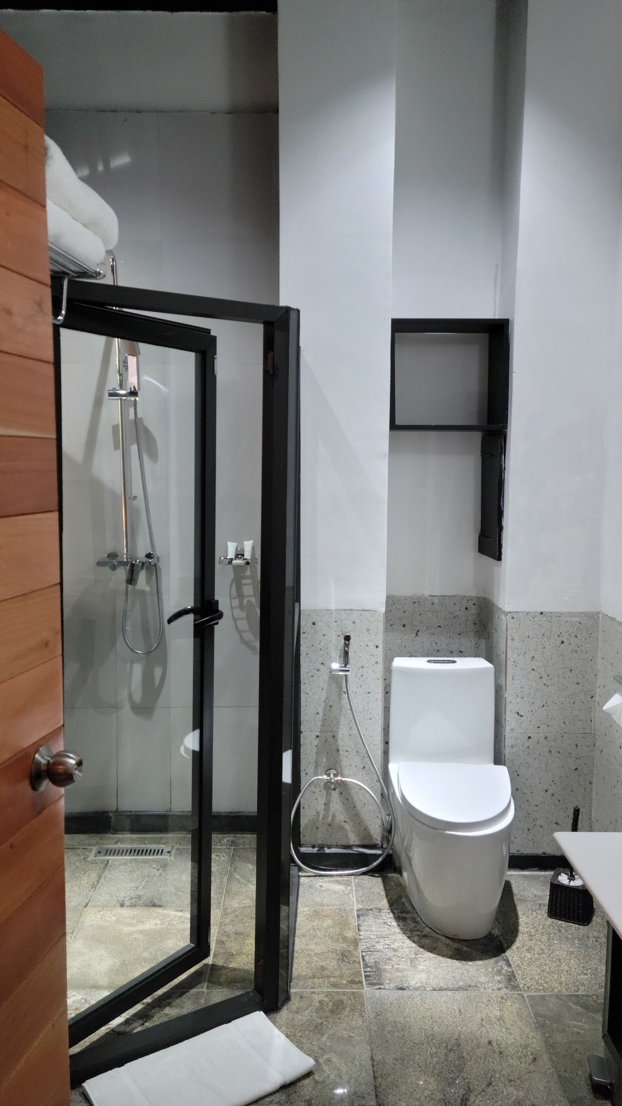 A bathroom with a glass-enclosed shower, a toilet, and a small shelf with toiletries.