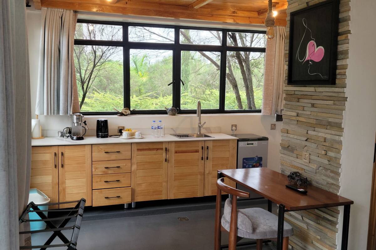 A modern kitchen with wooden cabinets, a sink, and a window with a view of trees.