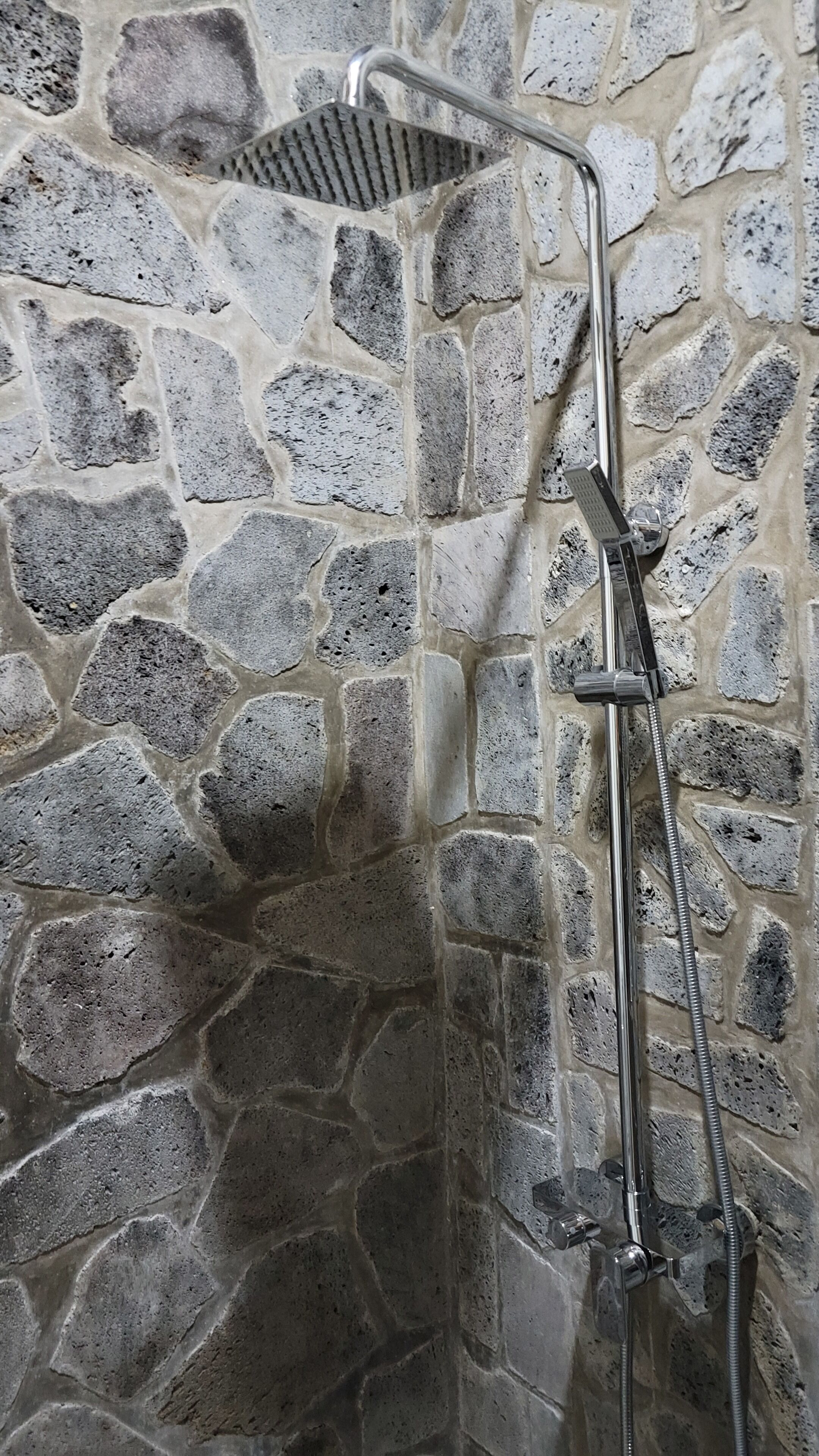 A shower with a stone wall backdrop.