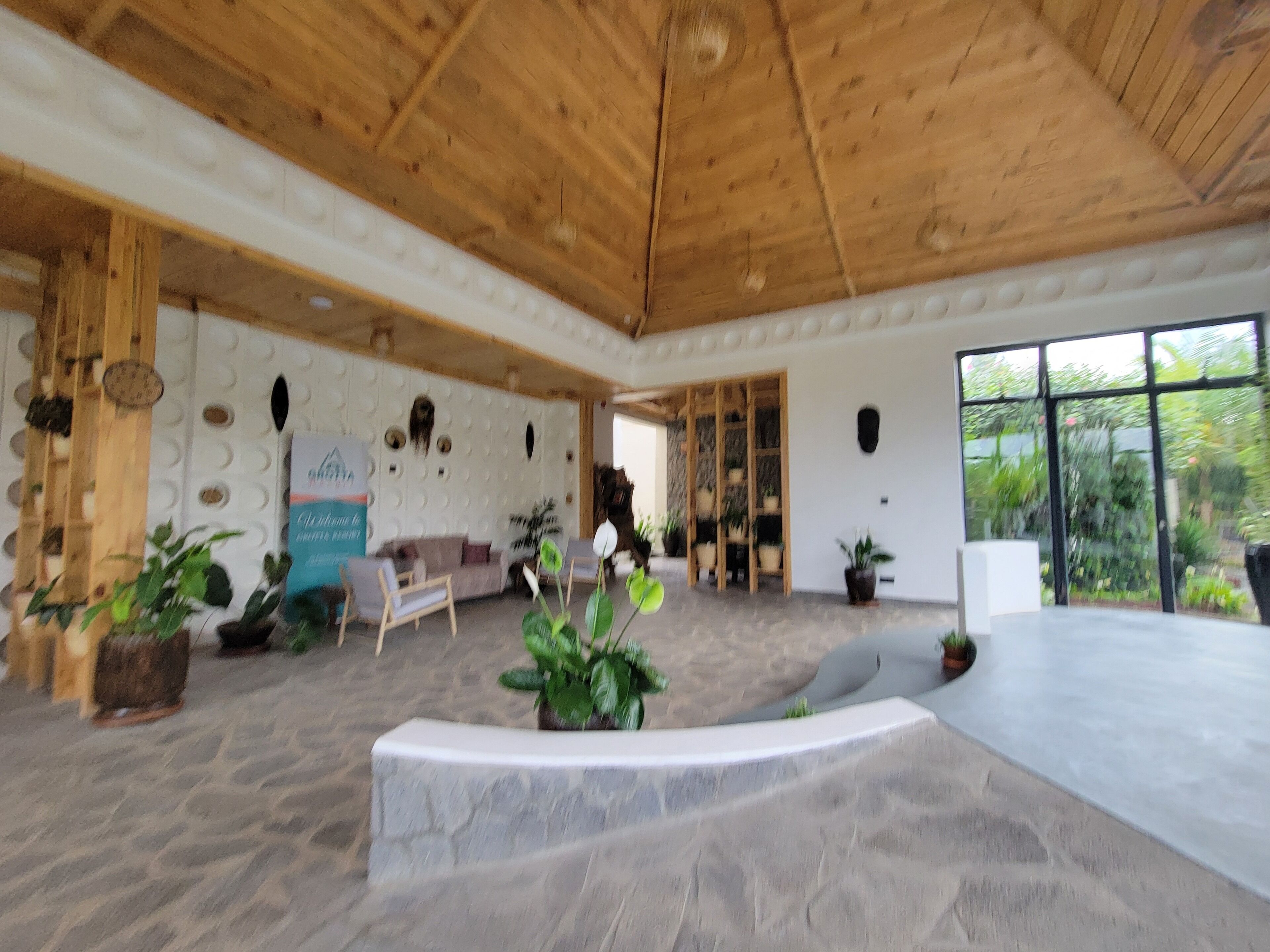 A spacious indoor area with a high wooden ceiling, a stone floor, and several potted plants.