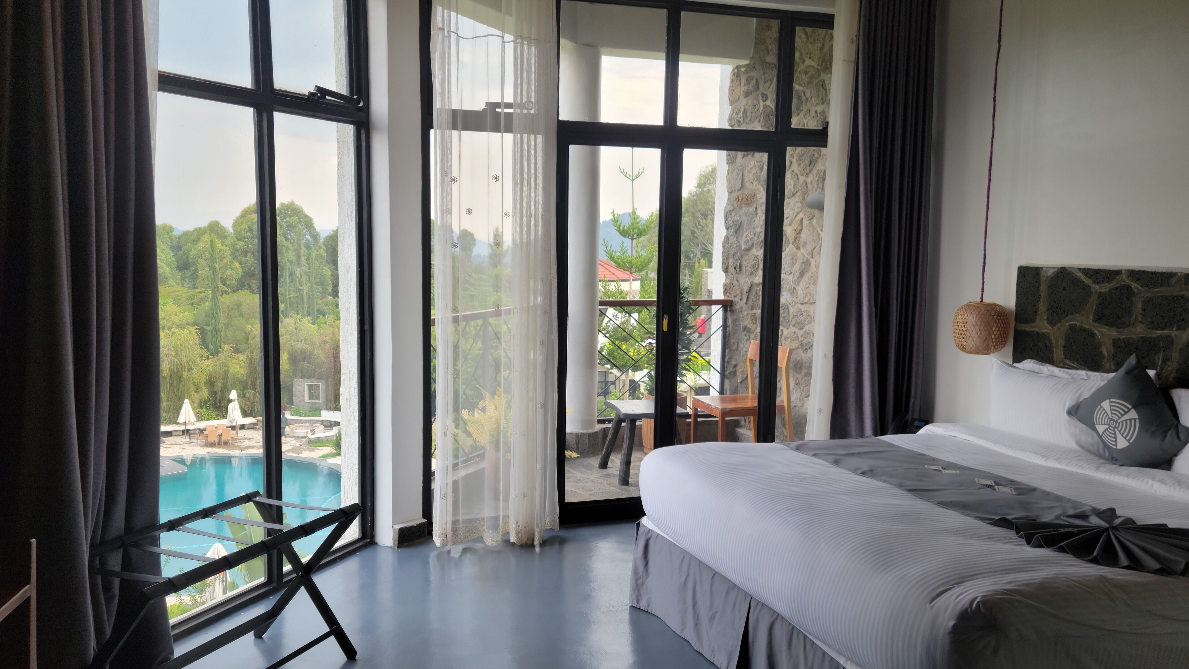 Un dormitorio con un ventanal grande, una cama y vistas a una piscina y follaje.