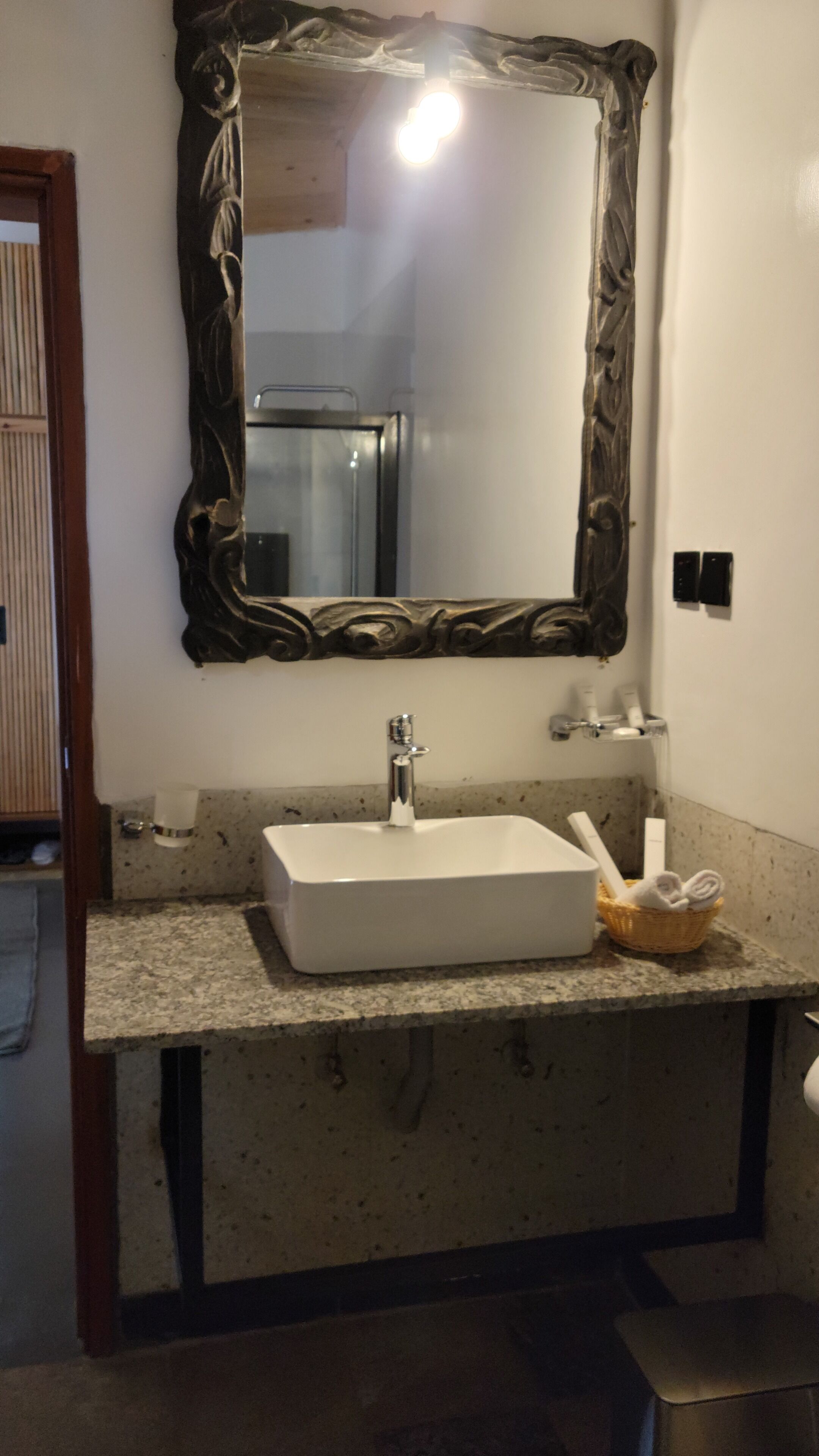 A bathroom with a white sink, a mirror with an ornate frame, and a small basket with towels.